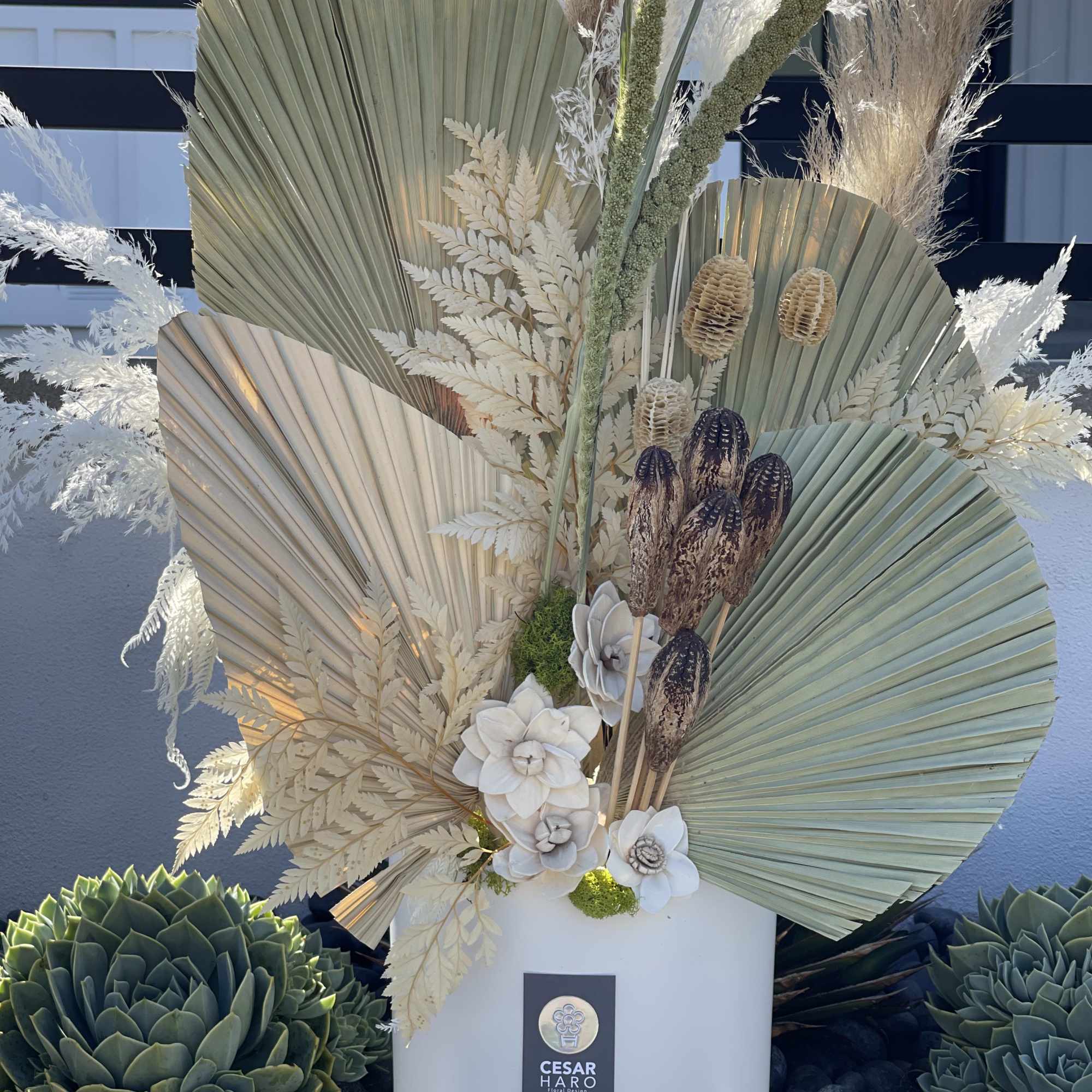 Tall arrangement with dried palm fans, white flowers, and pampas grass in a white vase.