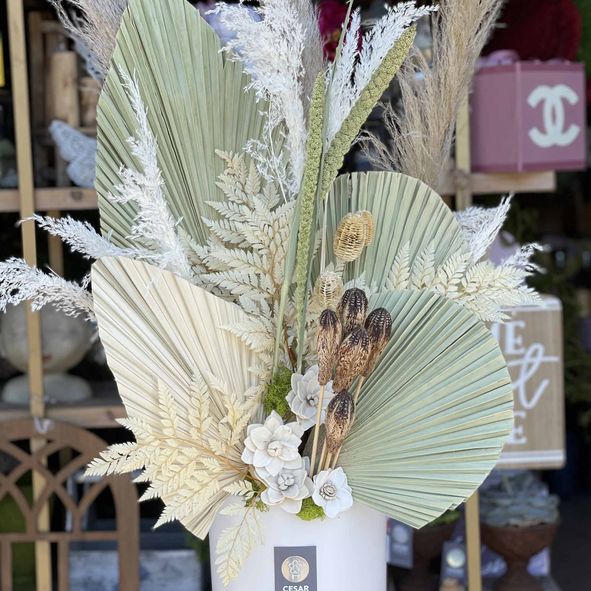 Tall dried floral arrangement in a white hatbox with fan-shaped palm leaves.