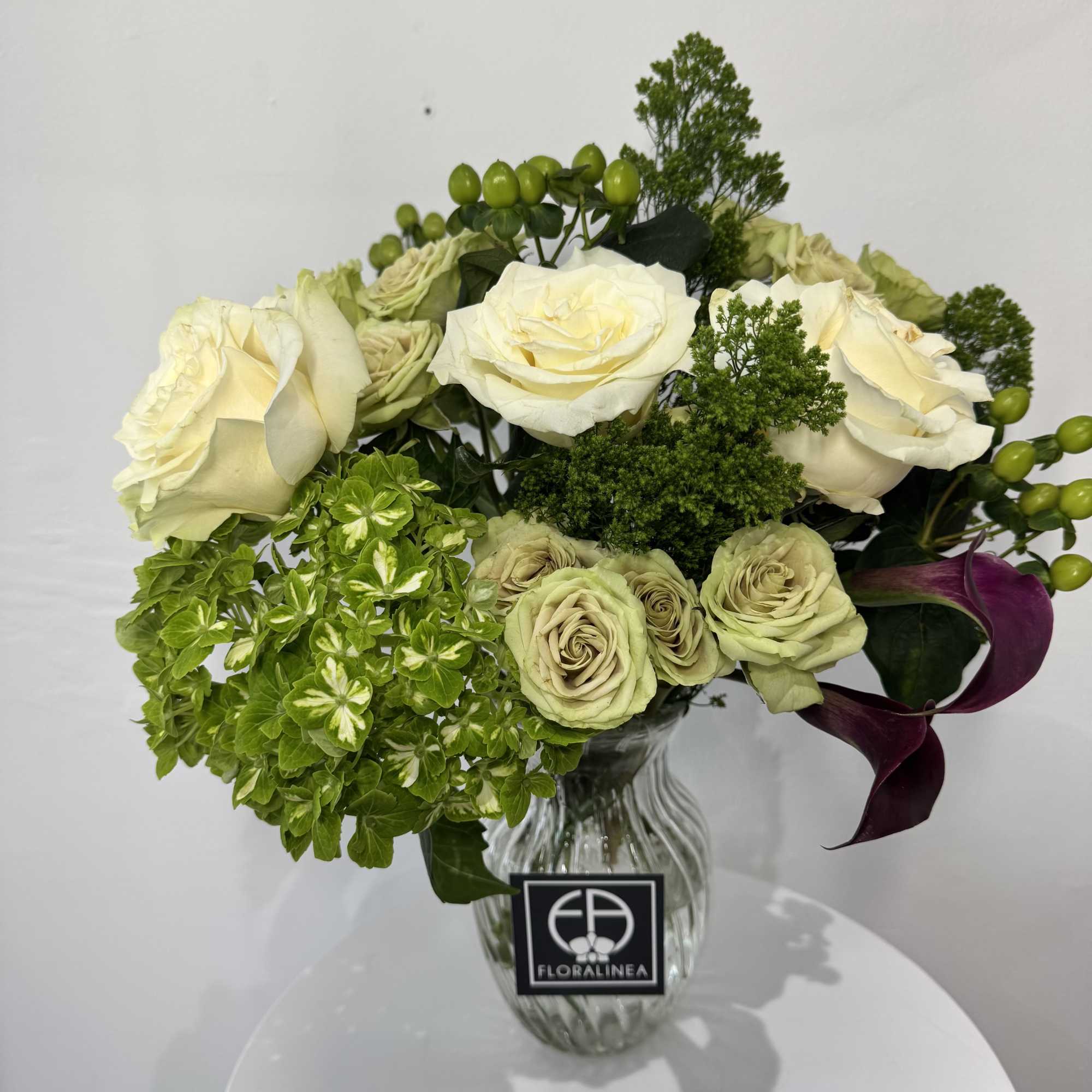 Cream roses and green hydrangea in a glass vase with purple calla lilies