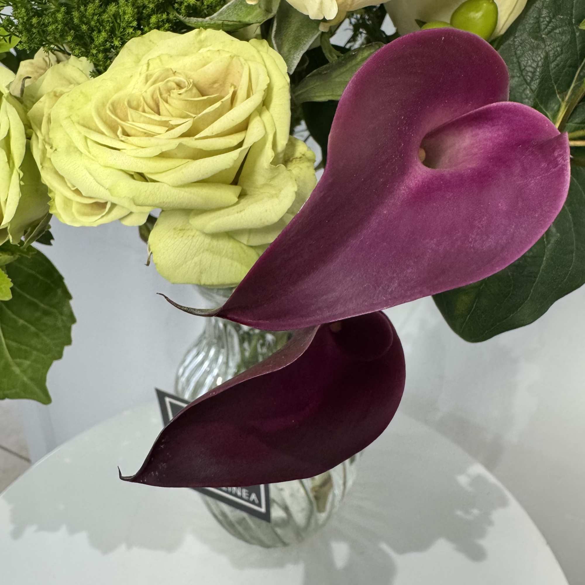 Bouquet of pale yellow roses and deep purple calla lilies in a glass vase