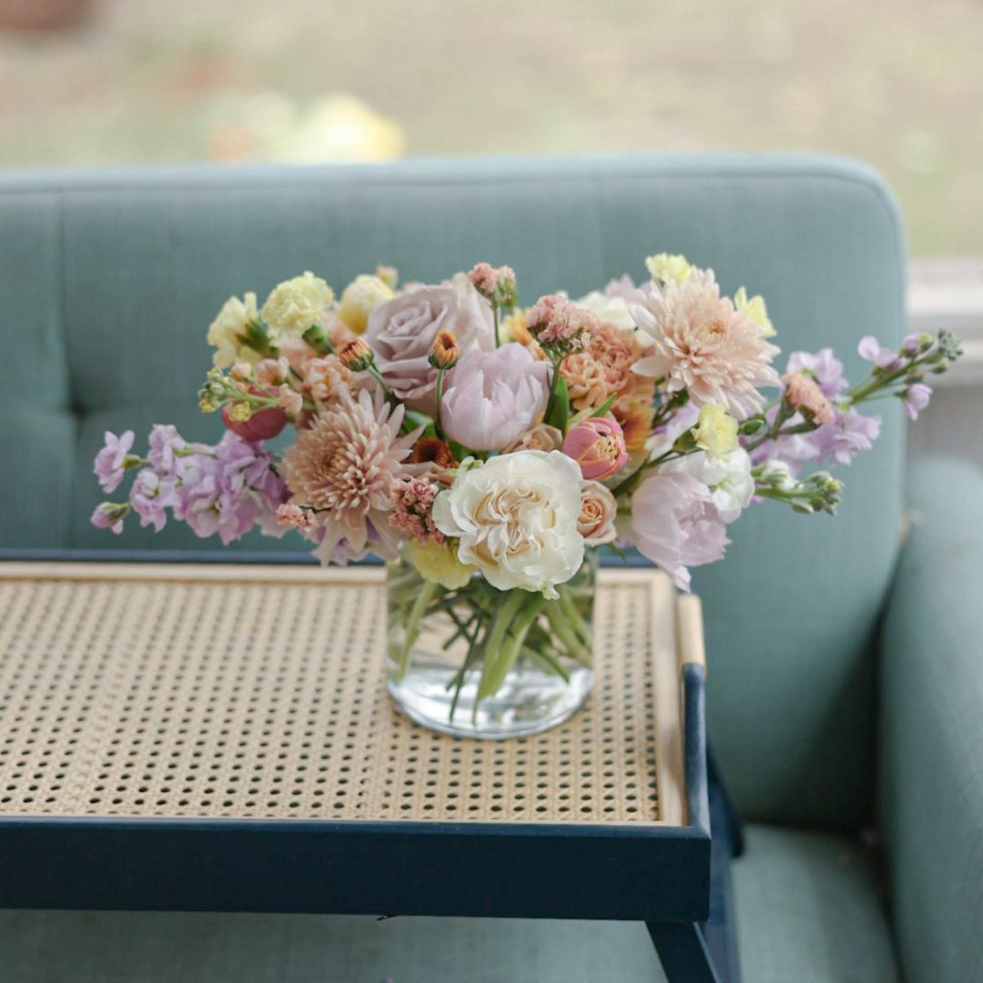 Pastel mixed flower bouquet in a clear glass vase on a tray table