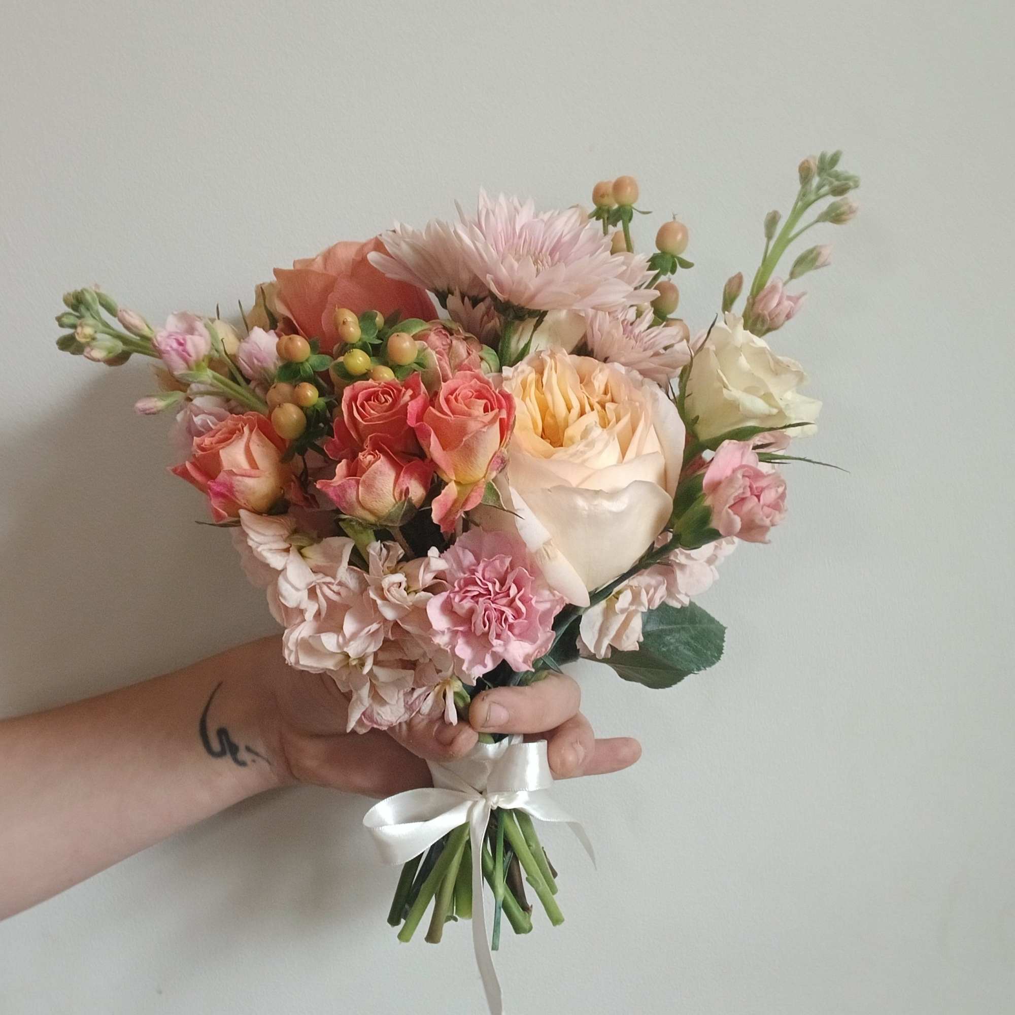 Handheld bouquet of pink and cream roses with pale blooms and a white ribbon