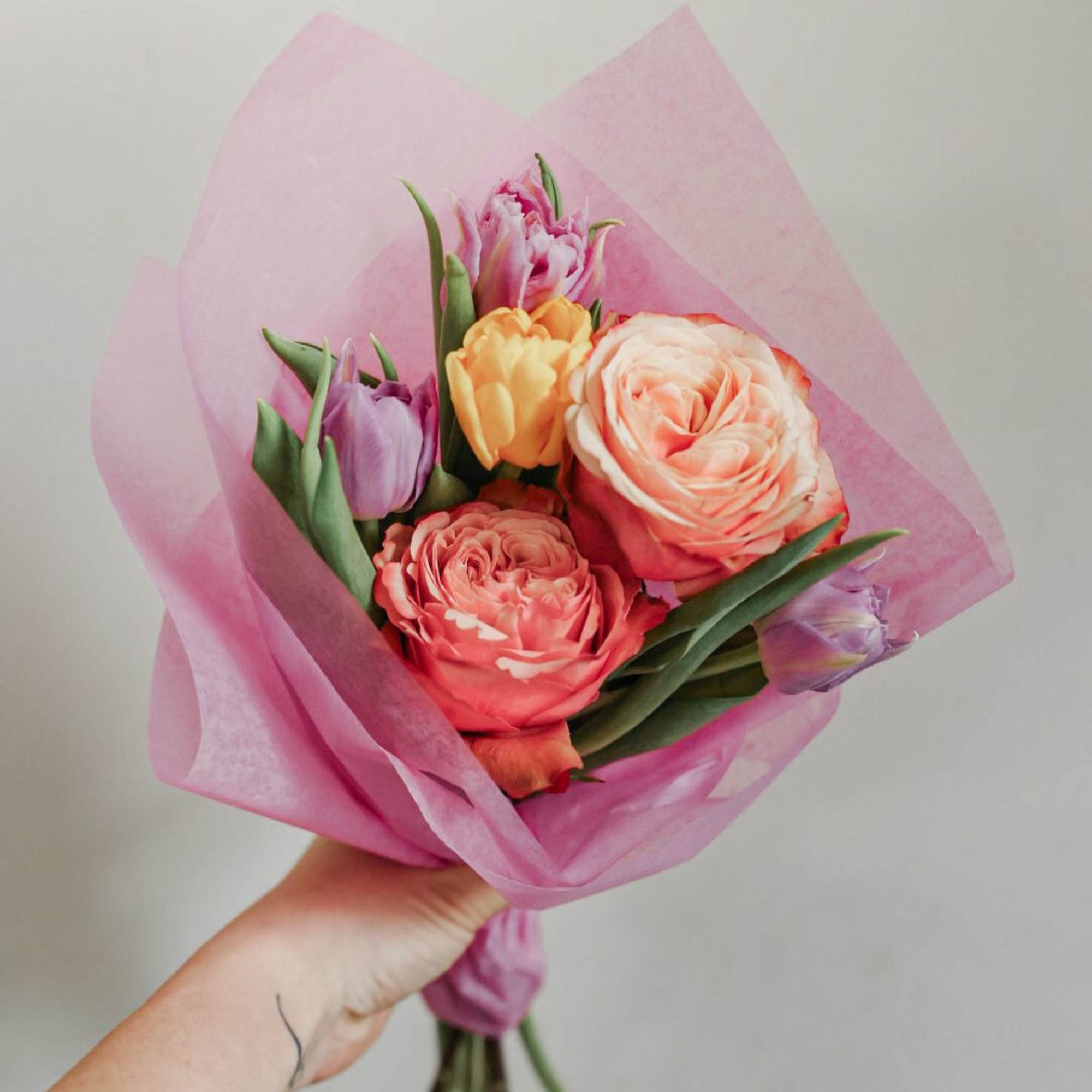 Handheld bouquet of pink and peach tulips wrapped in pink paper