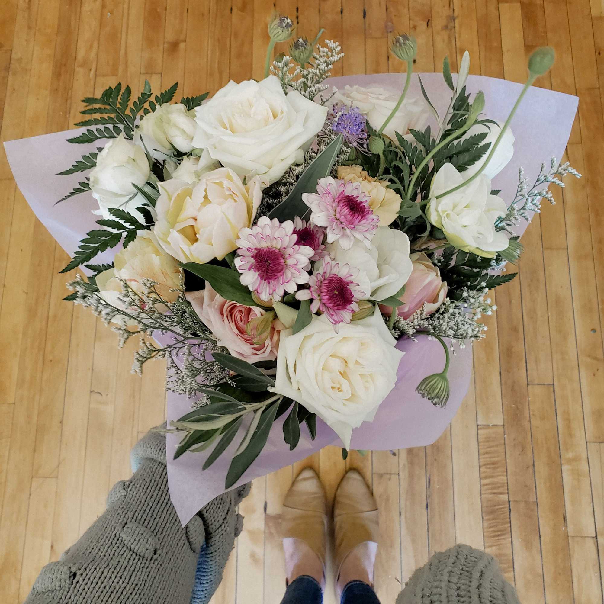 Handheld bouquet of white and blush flowers wrapped in lavender paper