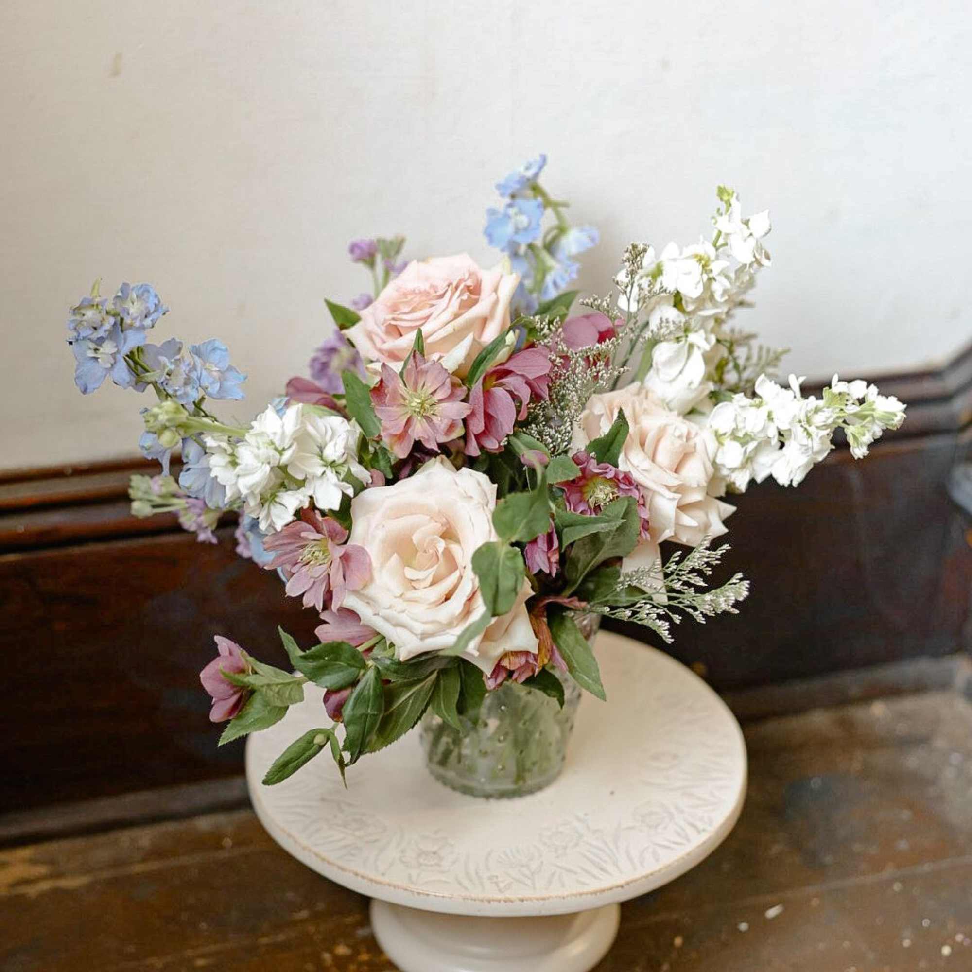 Pastel bouquet of roses and blue-white flowers in a glass vase