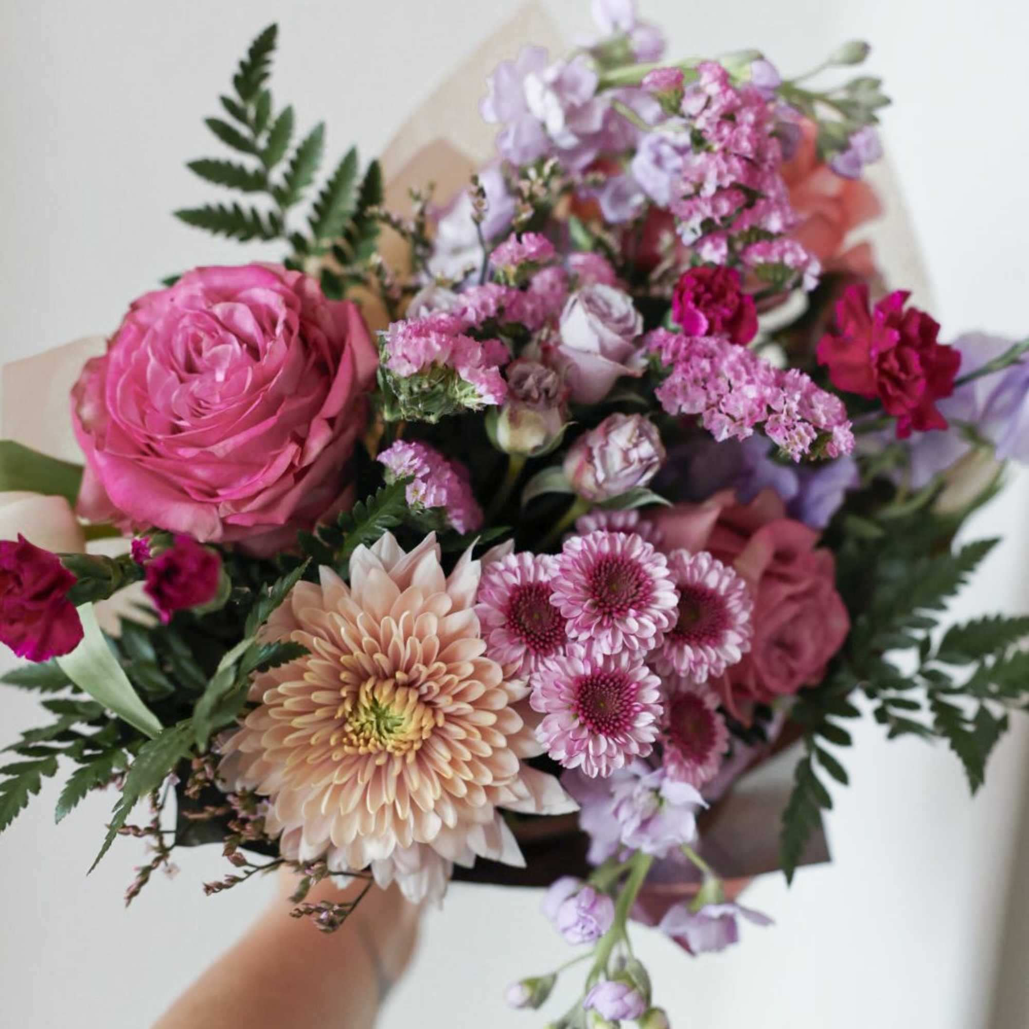 Handheld bouquet of pink and lavender flowers with mixed blooms