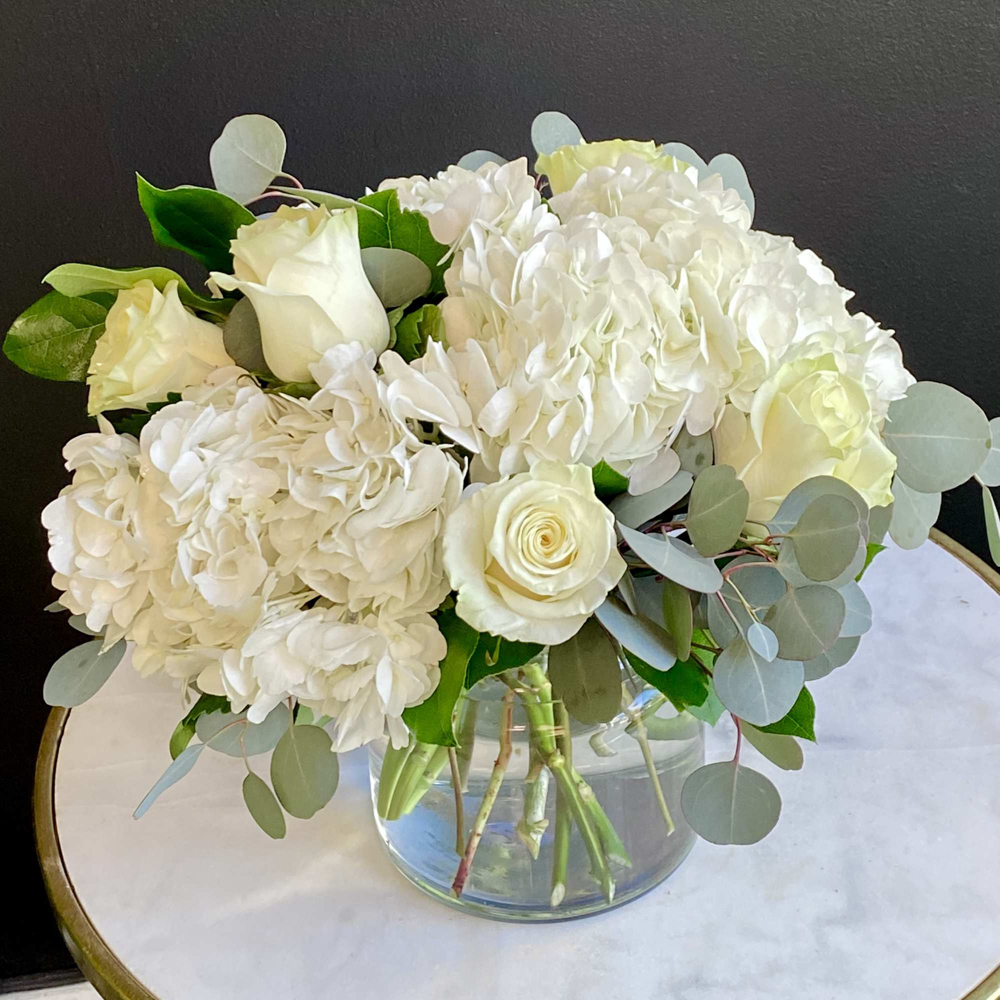 White roses and hydrangeas in a clear glass vase with eucalyptus