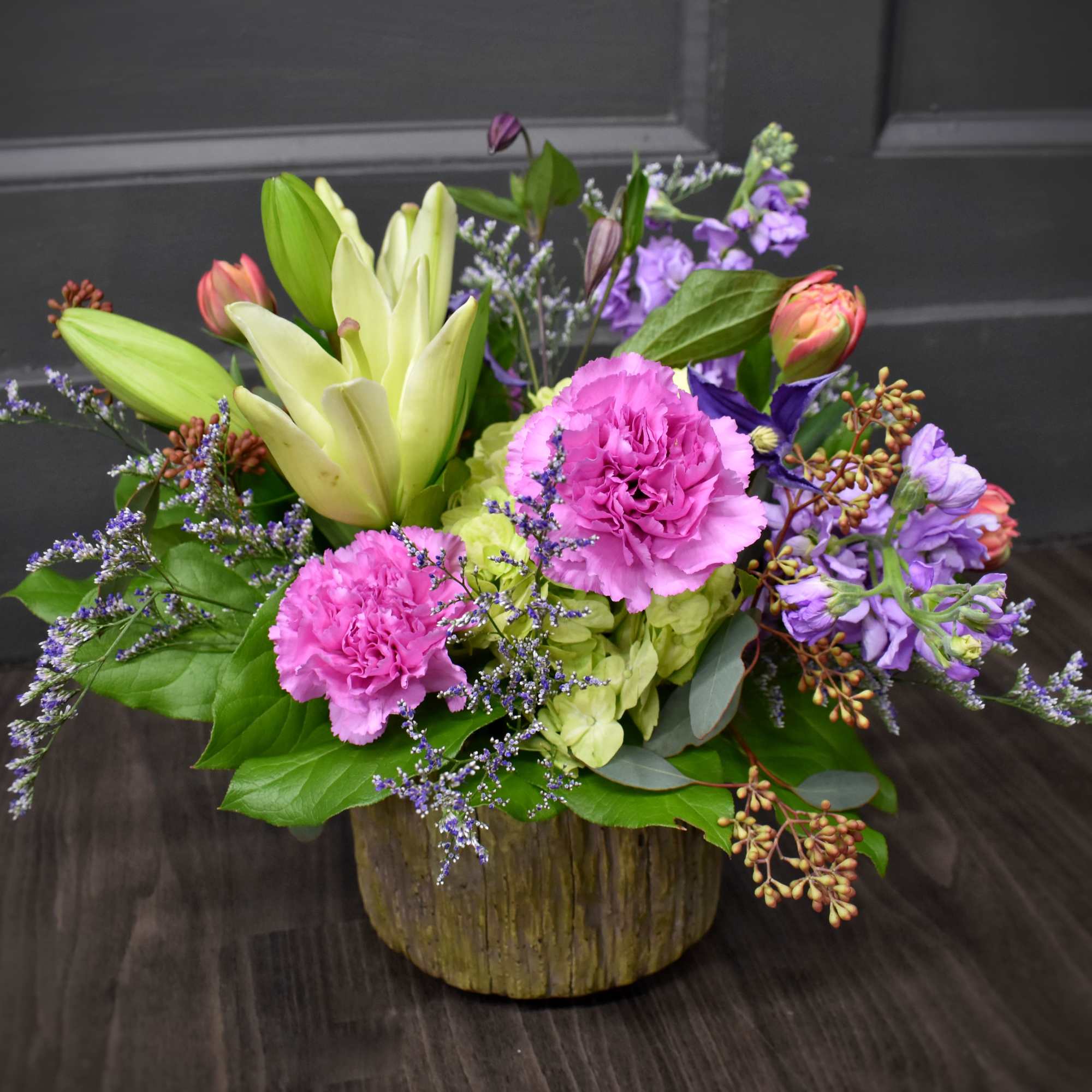 Mixed bouquet with pink carnations, lilies, and purple flowers in a wooden container