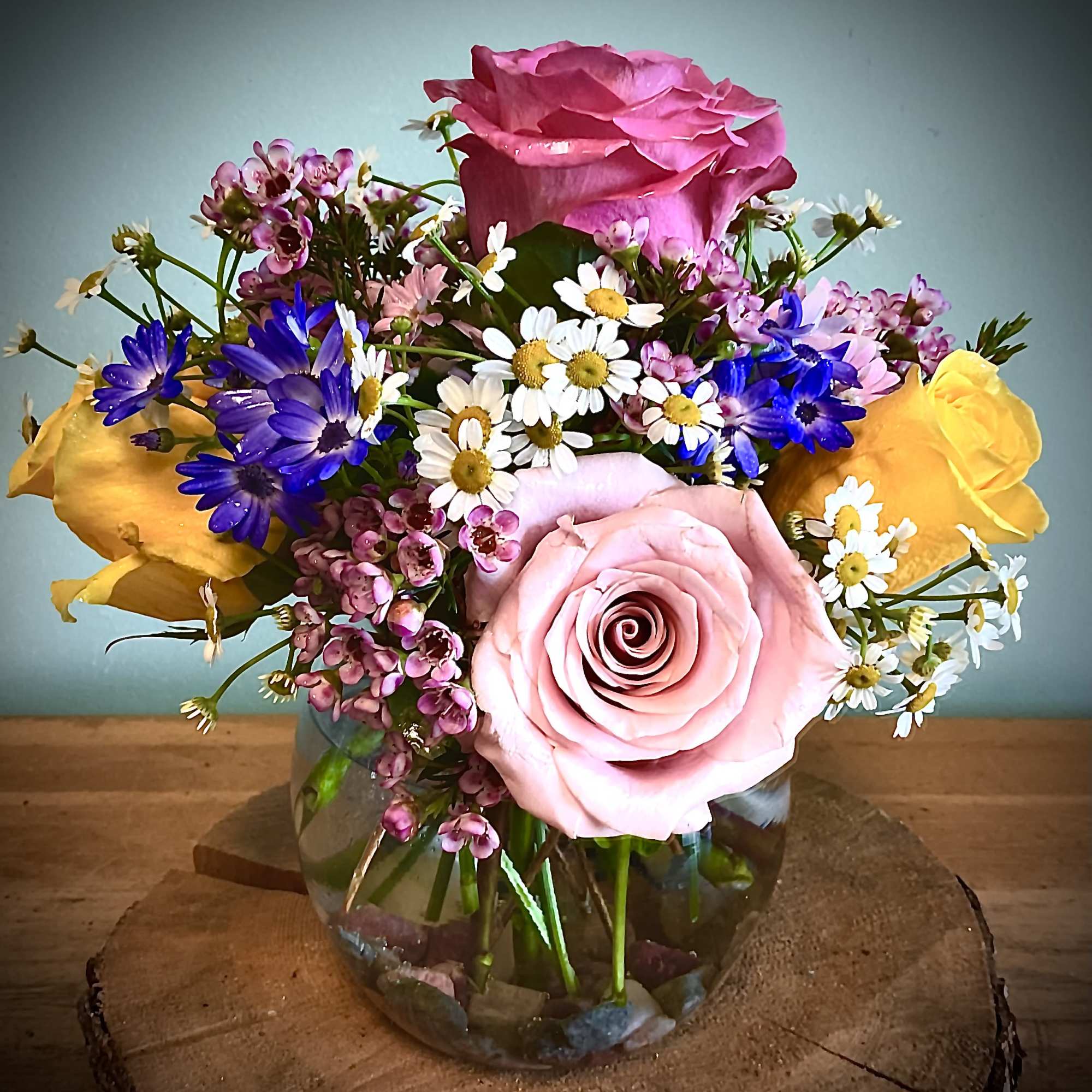 Mixed bouquet of pink and yellow roses with small daisy flowers in a glass vase