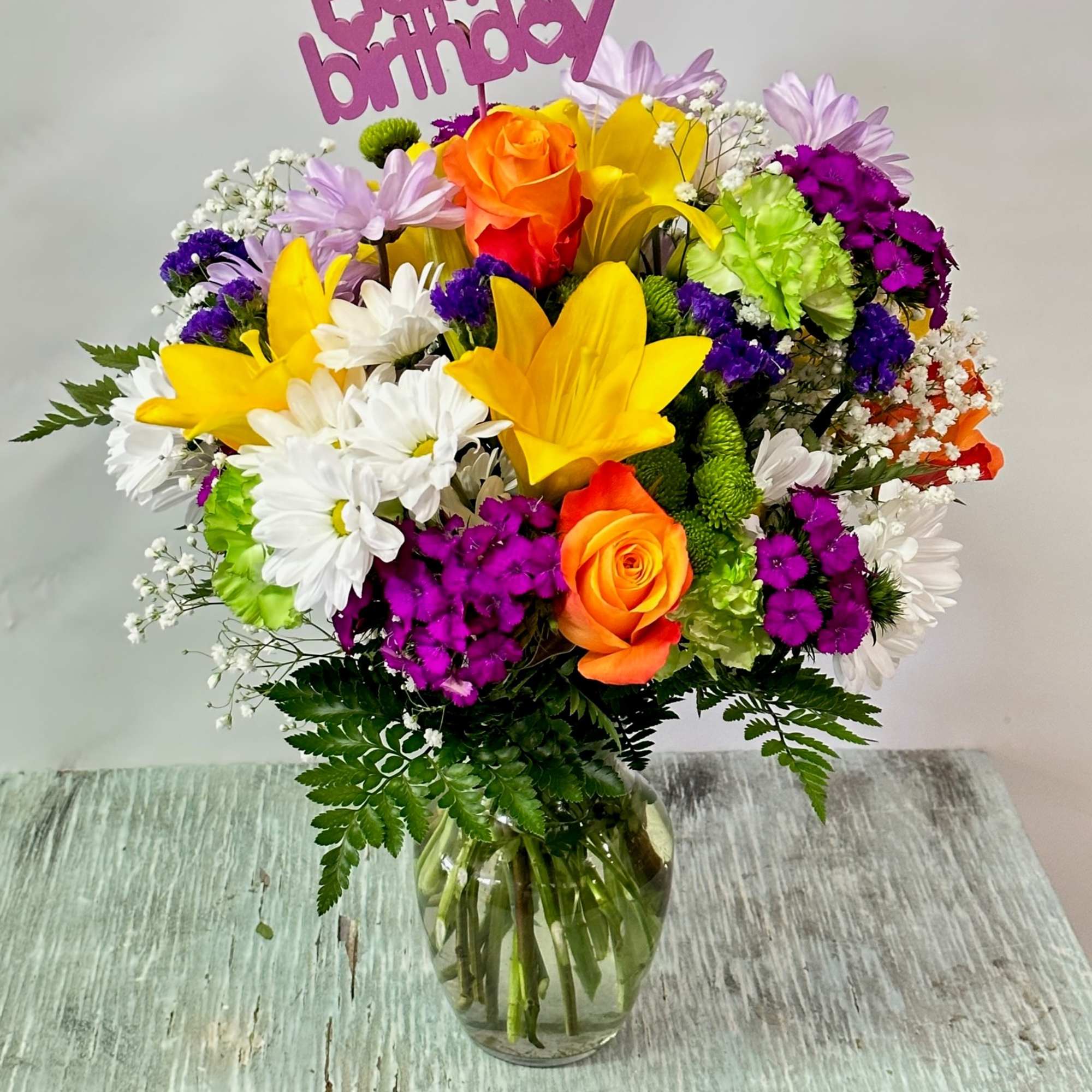 Colorful birthday bouquet in a glass vase with a "Happy birthday" topper