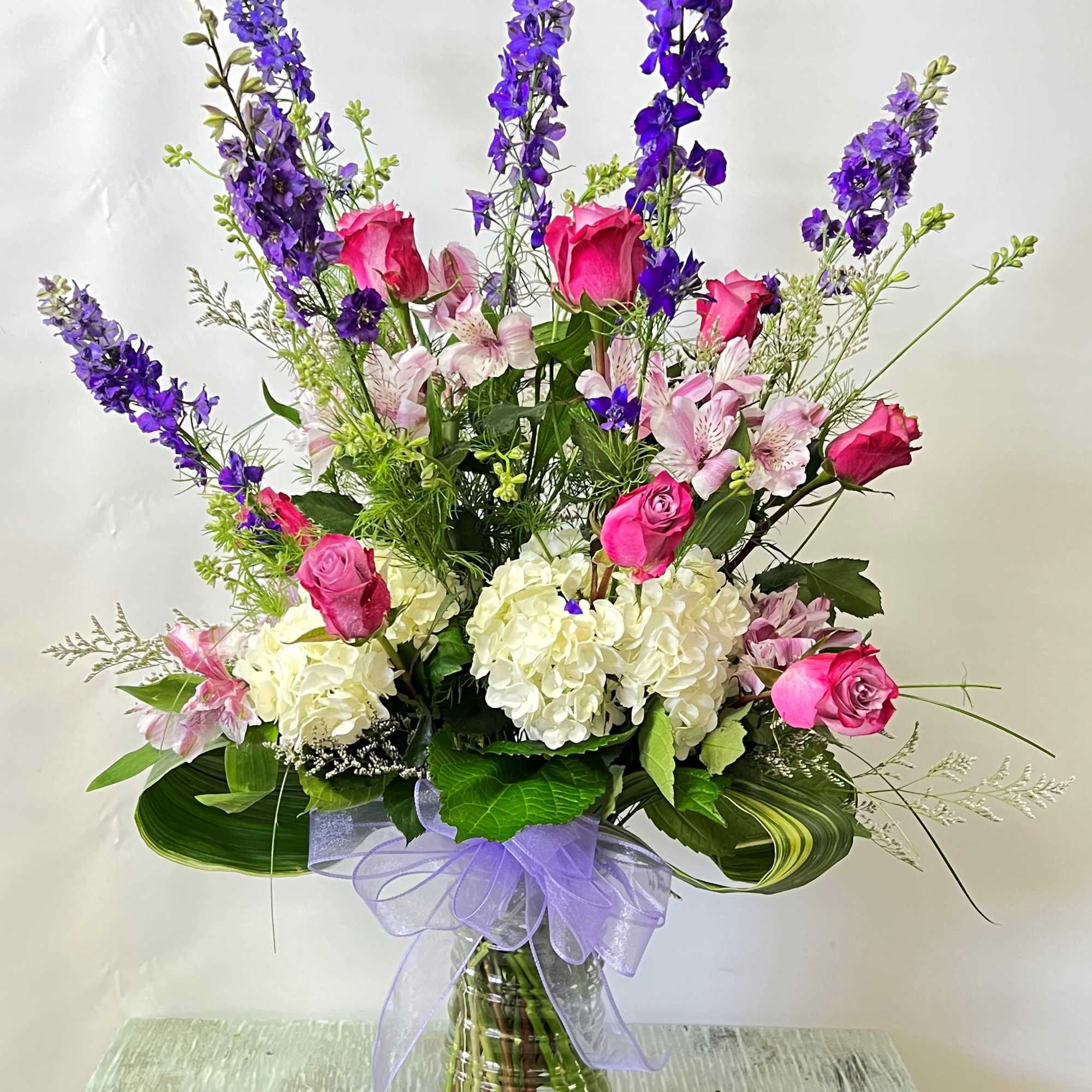 Tall bouquet of pink roses, white hydrangeas, and purple delphinium in a glass vase