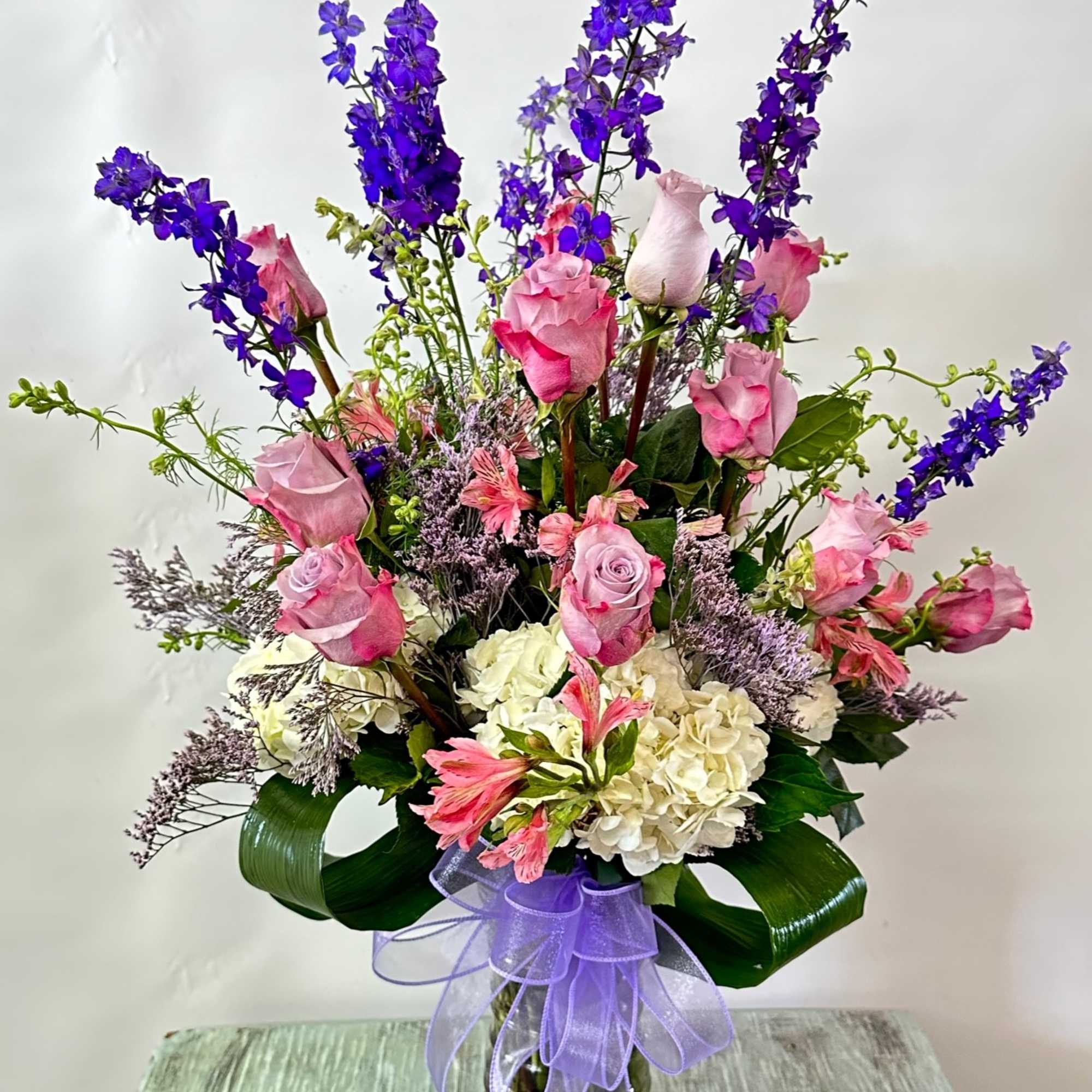 Tall bouquet of pink roses, white hydrangeas, and purple flowers in a glass vase