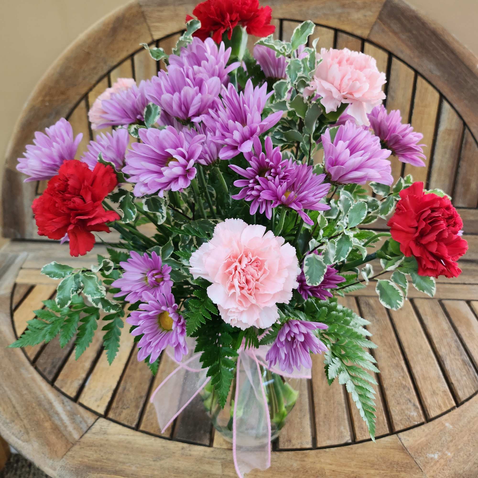 Bouquet of purple and pink flowers in a clear vase with a ribbon