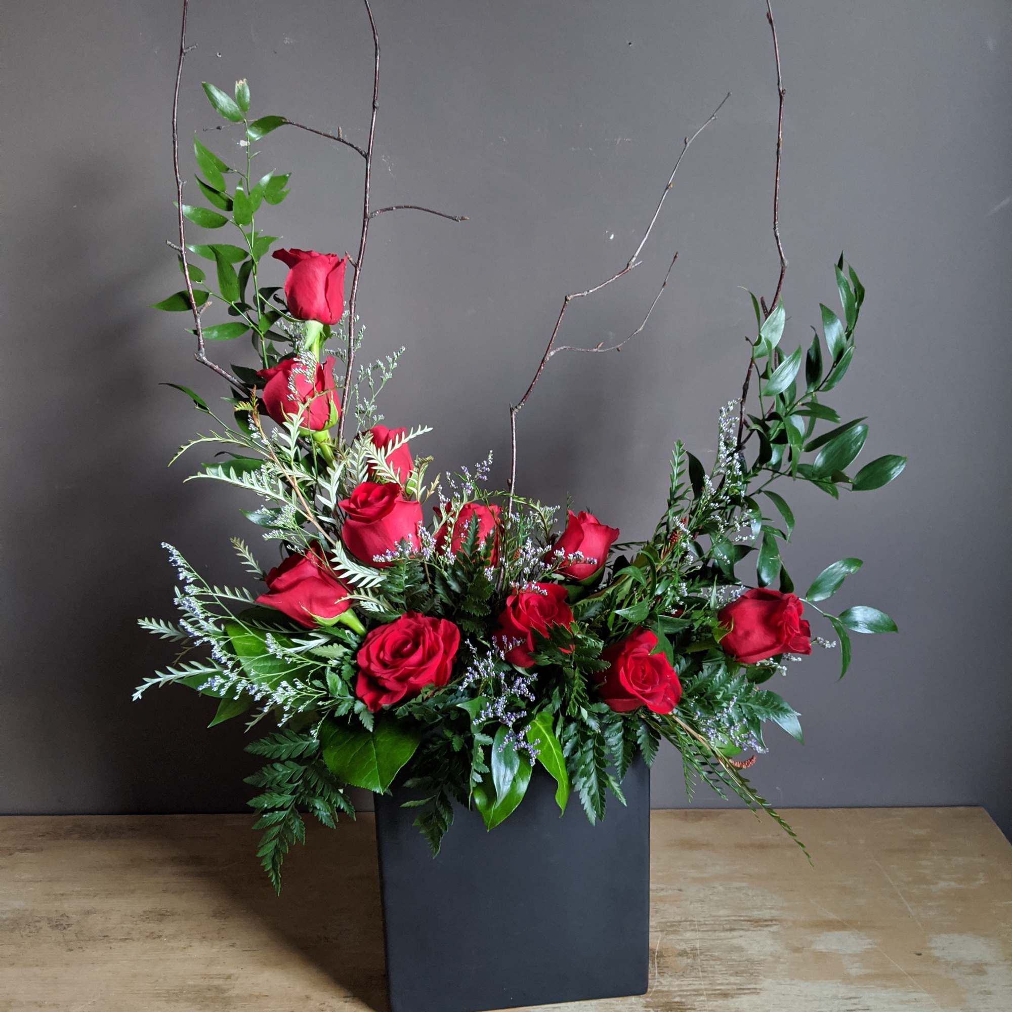 Red roses arranged in a black square vase with tall branches