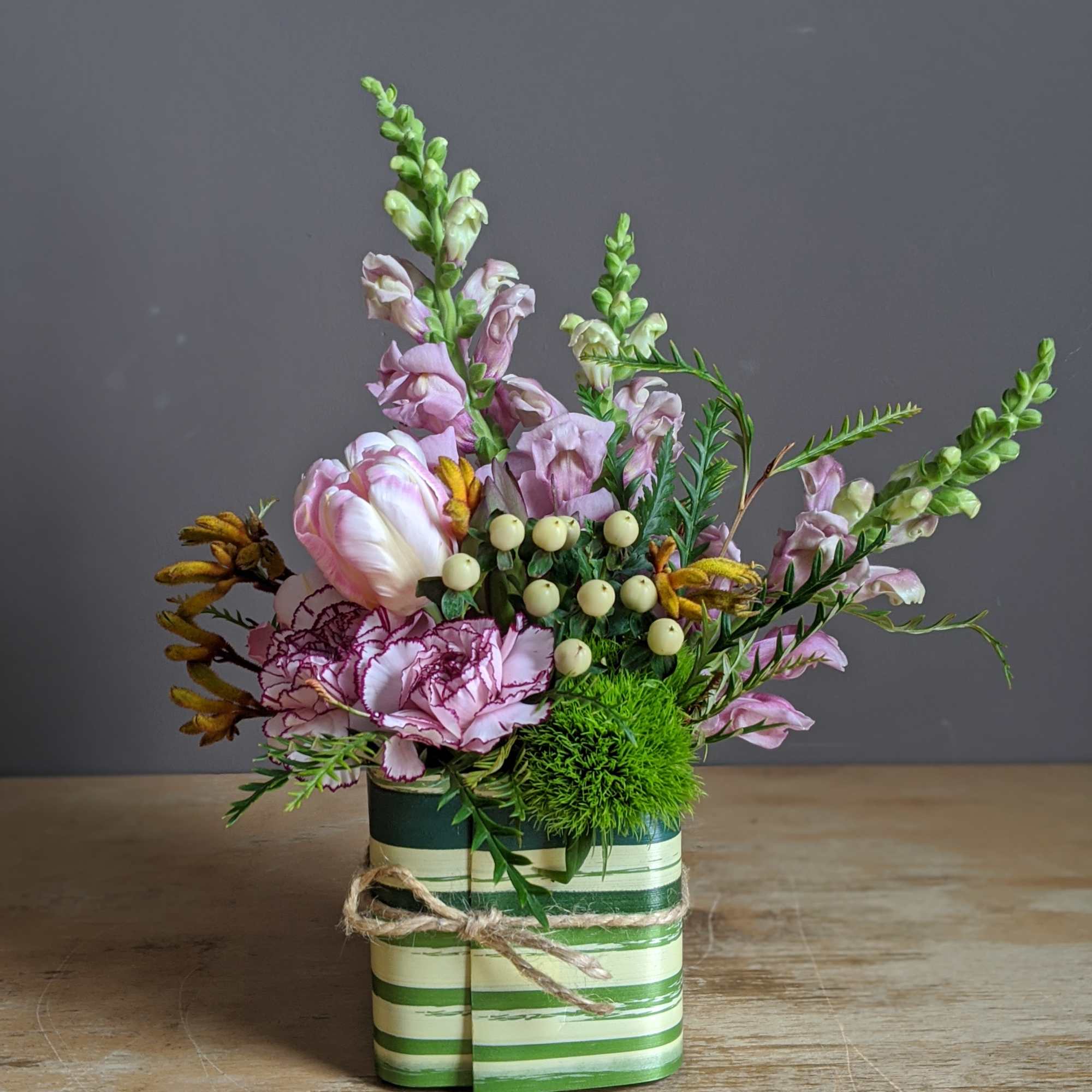 Pink and white floral arrangement in a striped green container