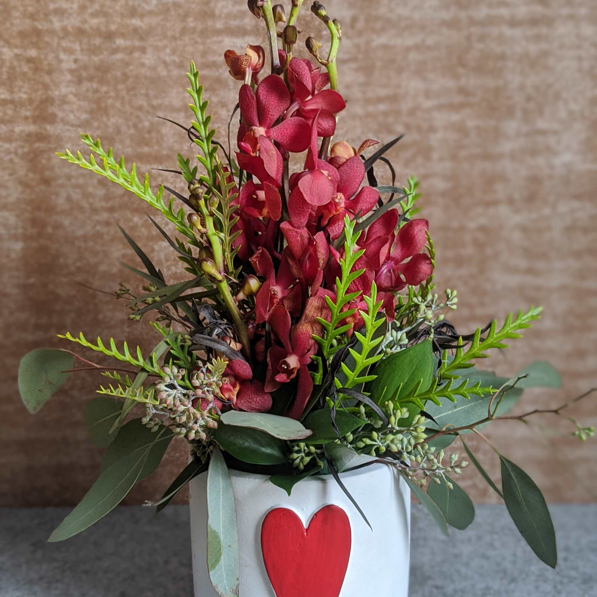 Red orchid arrangement in a white pot with a red heart