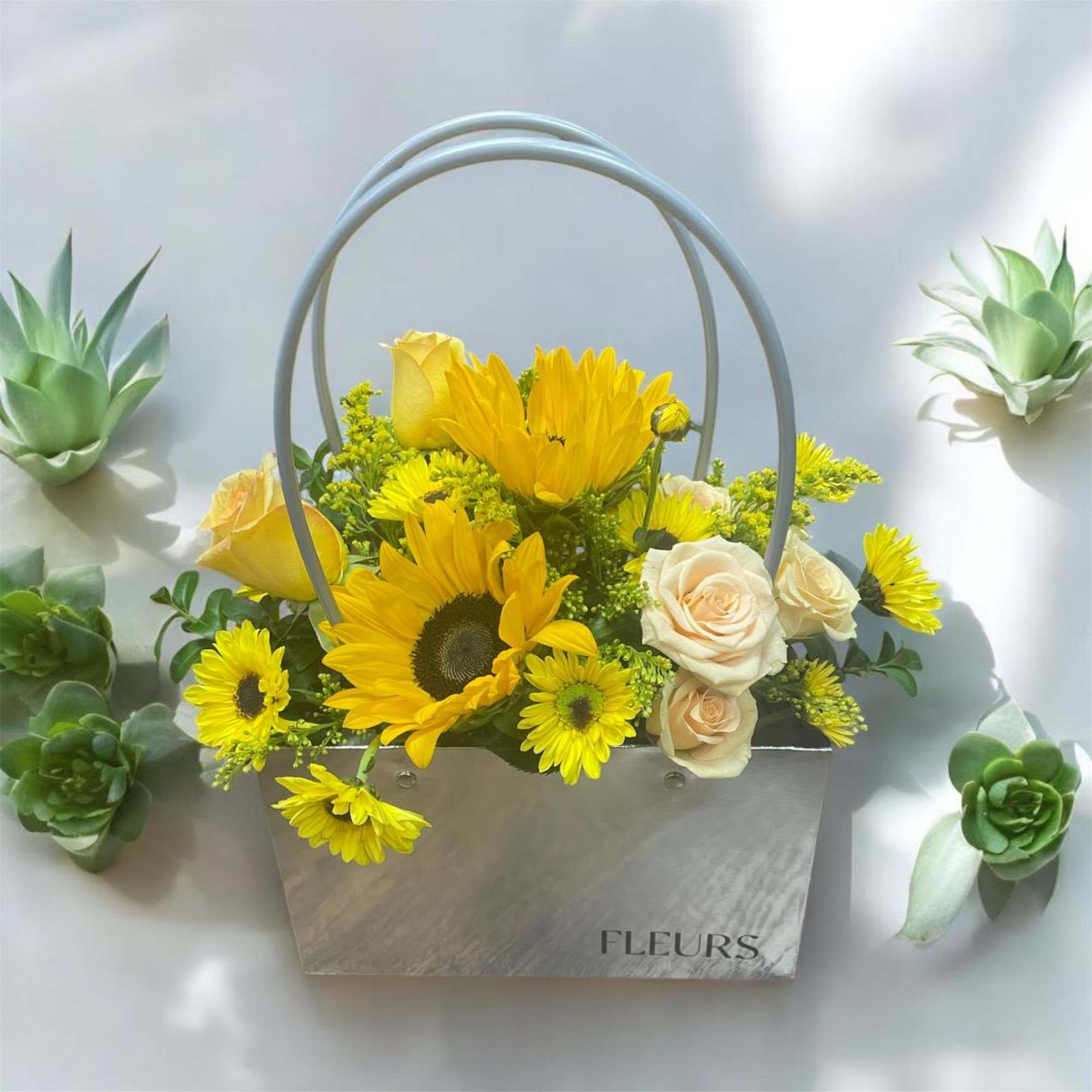 Yellow and cream flowers arranged in a metal basket with arched handles