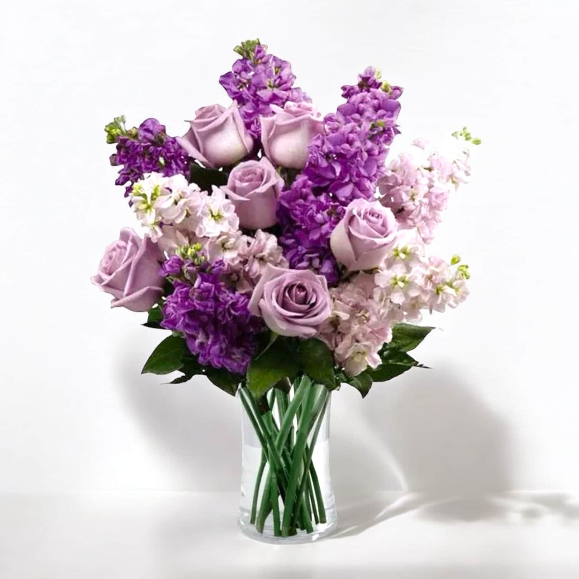 Lavender roses and purple flowers in a clear glass vase