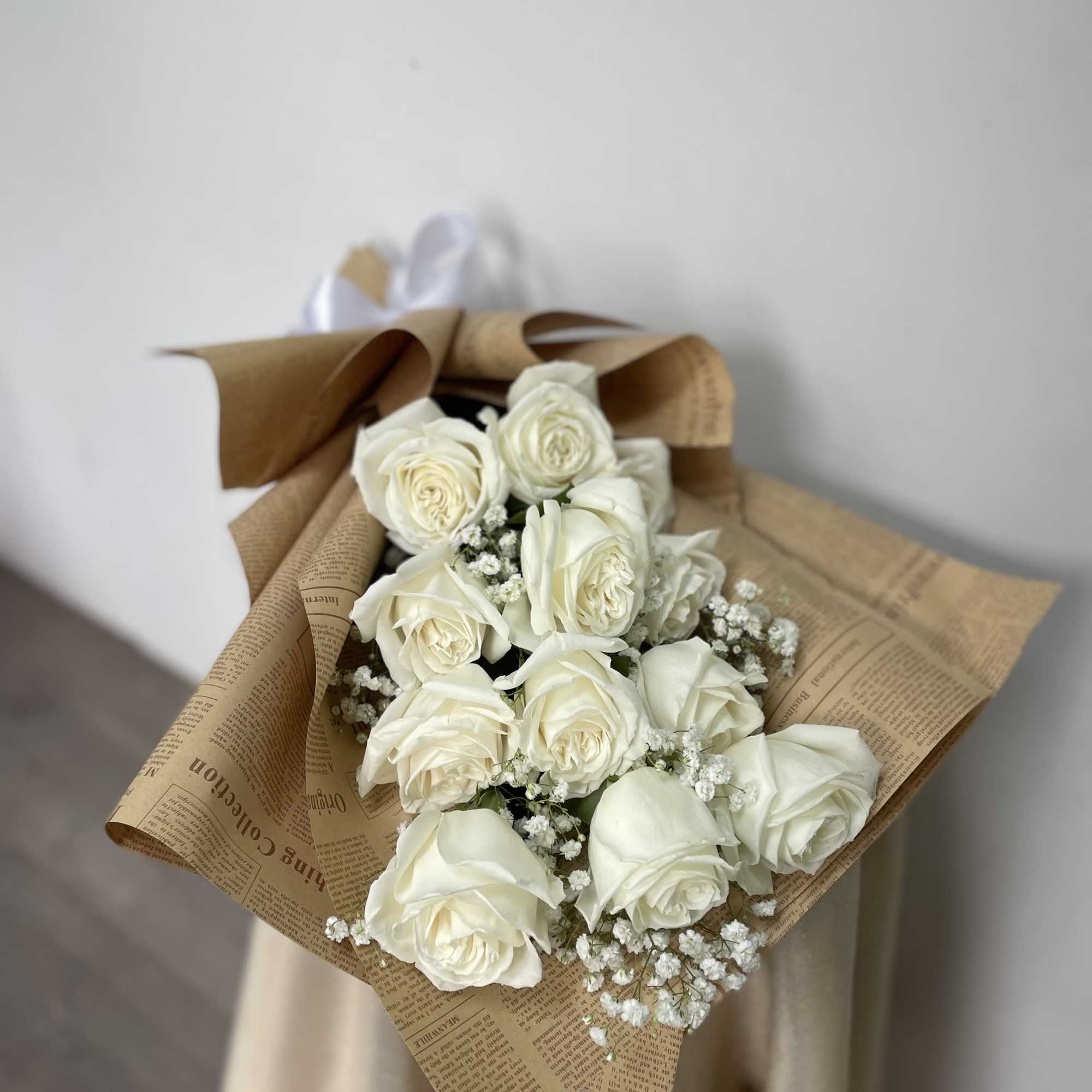 Bouquet of white roses wrapped in brown paper with small white filler flowers
