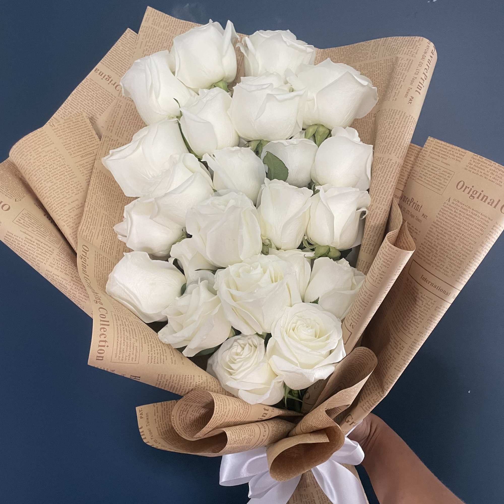 Bouquet of white roses wrapped in brown paper with a white ribbon
