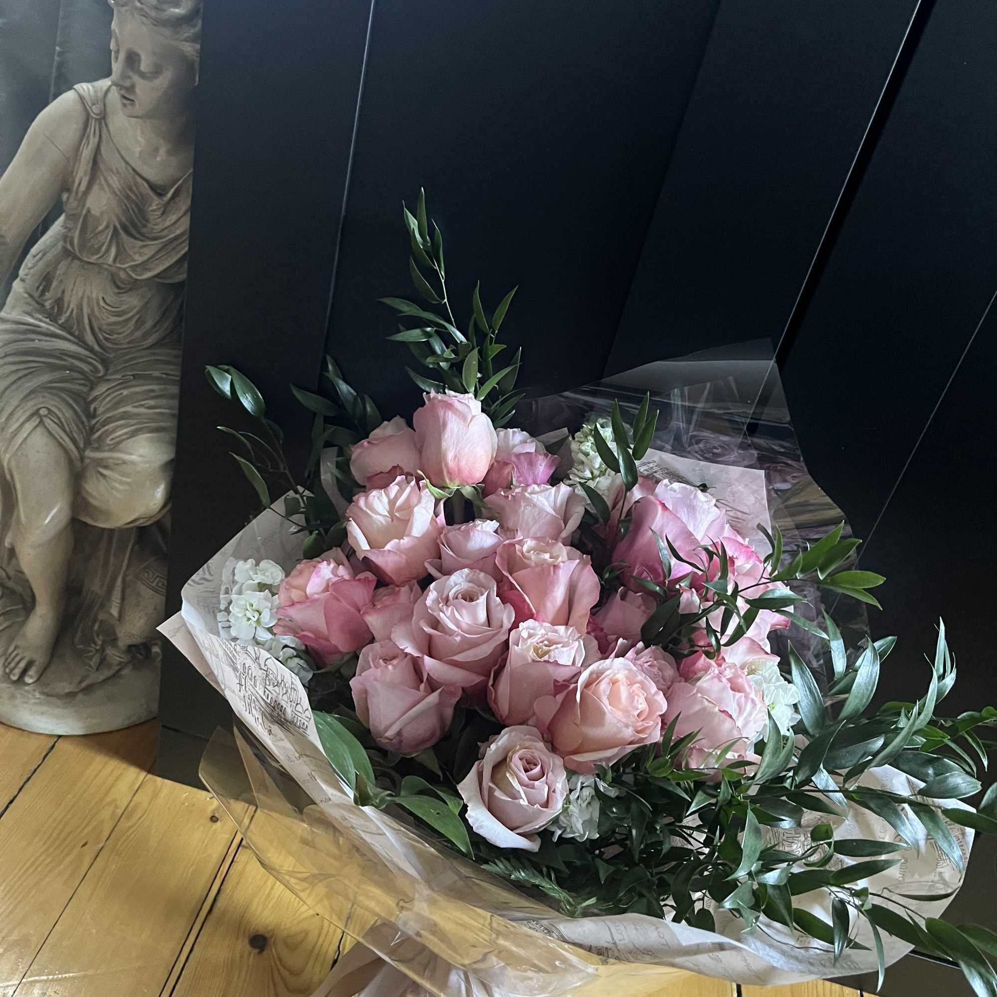 Bouquet of pale pink roses with greenery wrapped in clear paper