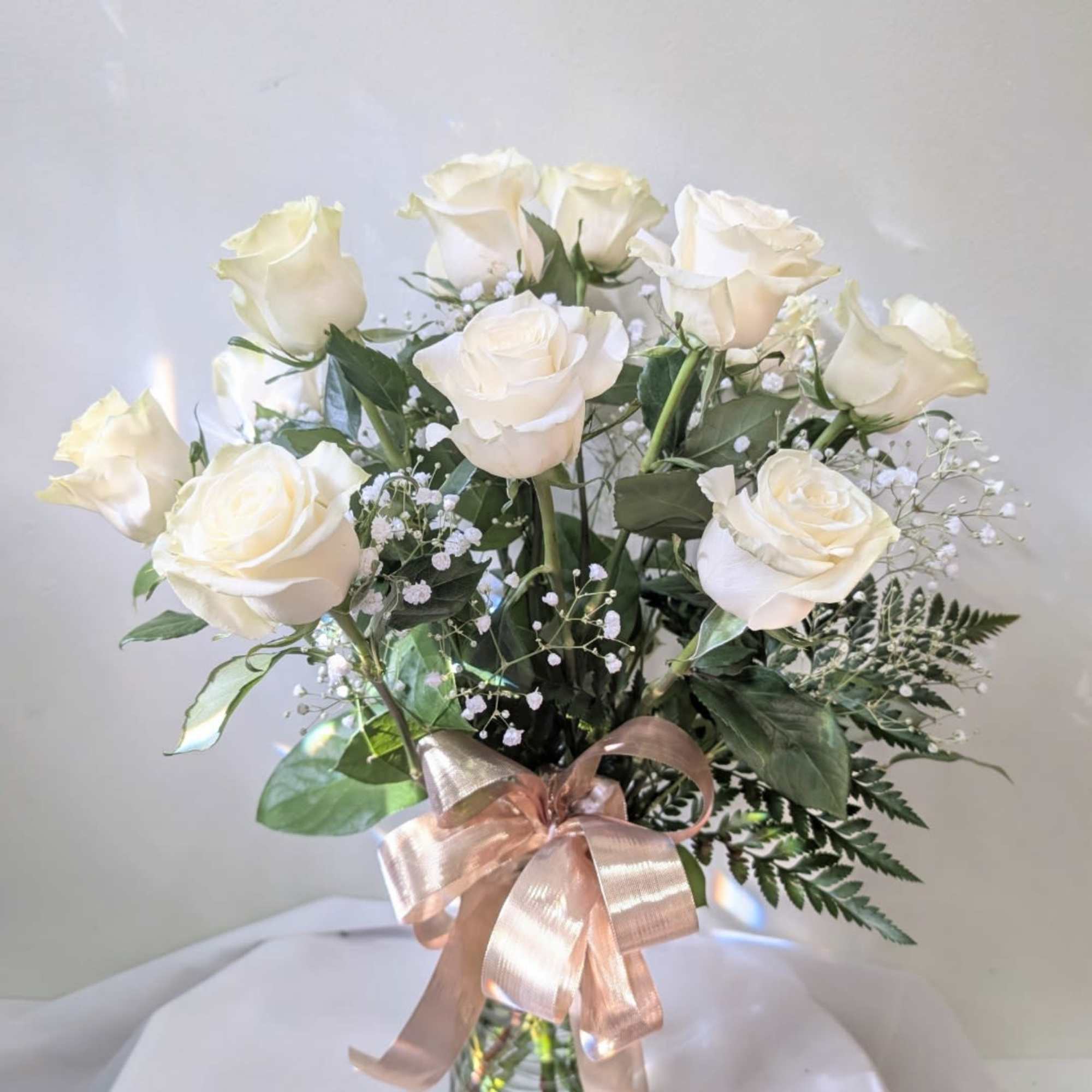 White roses in a glass vase with a pink ribbon