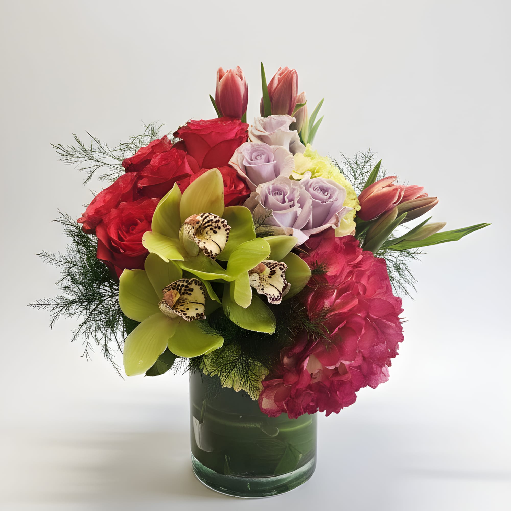 Mixed bouquet of roses, orchids, tulips, and hydrangeas in a glass vase