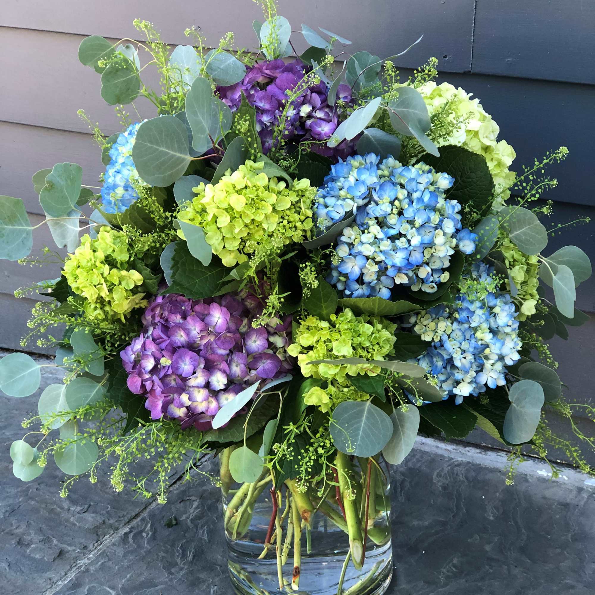 Bouquet of blue, purple, and green hydrangeas in a glass vase