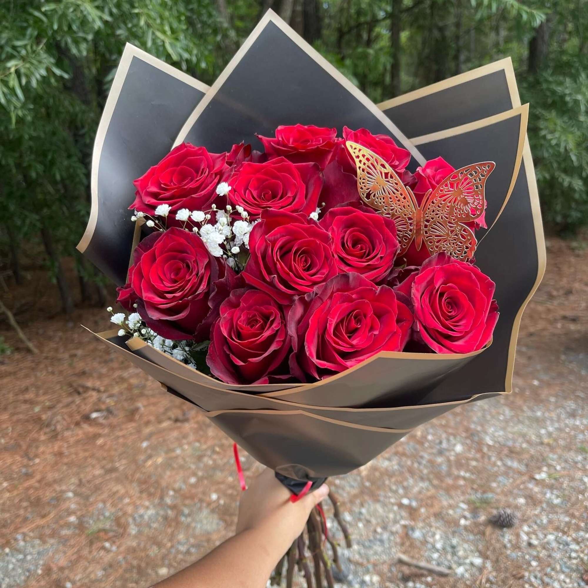 Bouquet of red roses wrapped in black paper with a butterfly accent