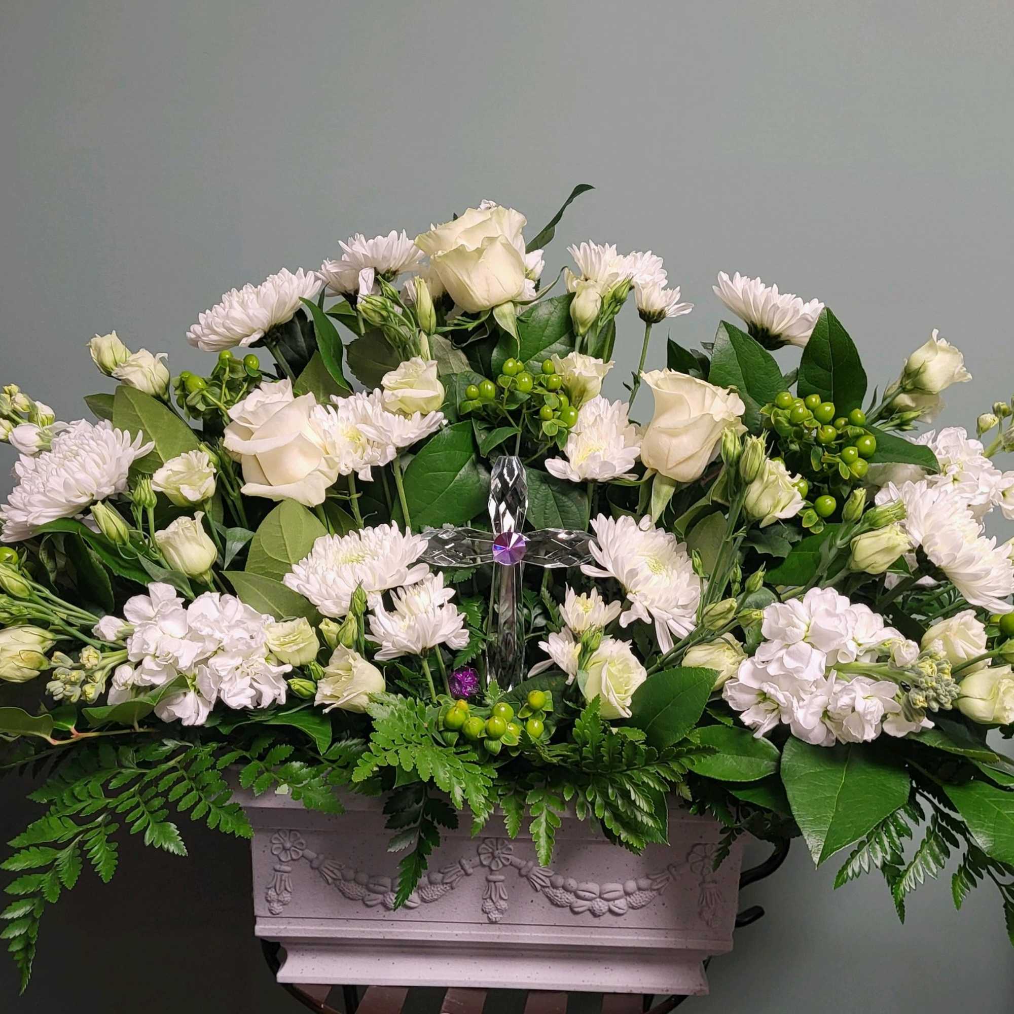 White floral arrangement in a decorative rectangular planter with a clear cross centerpiece