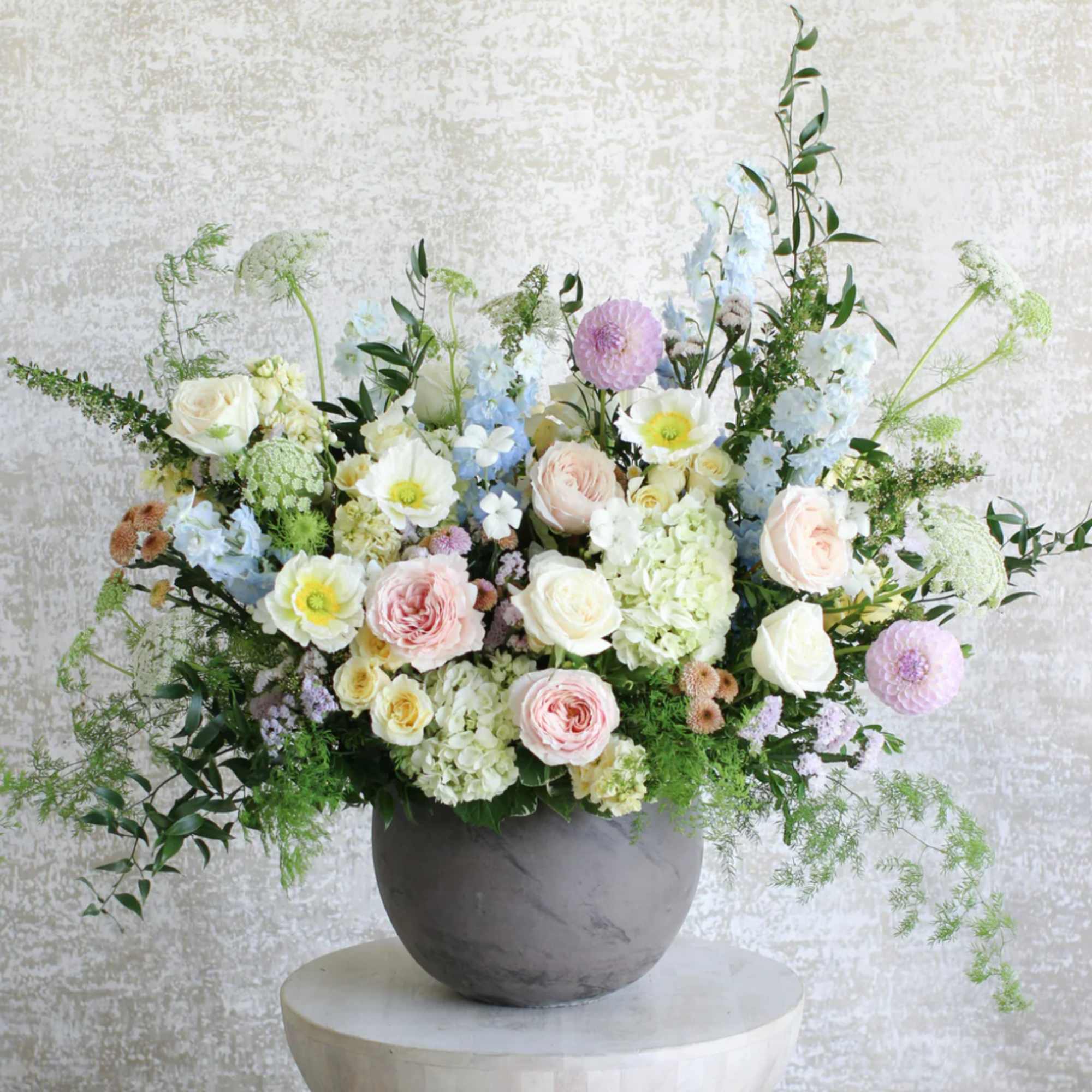 Large pastel arrangement of roses, hydrangeas and mixed blooms in a gray bowl vase on a pedestal table