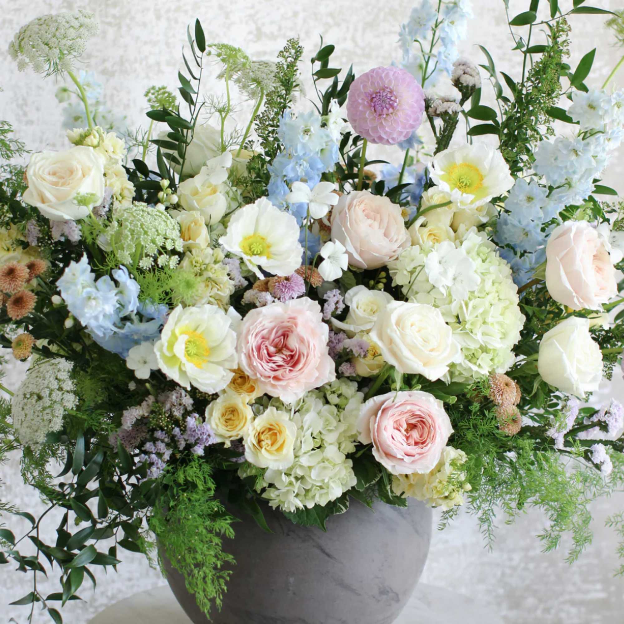 Large garden-style arrangement of blush and cream roses, white poppies, and pastel blooms in a gray bowl