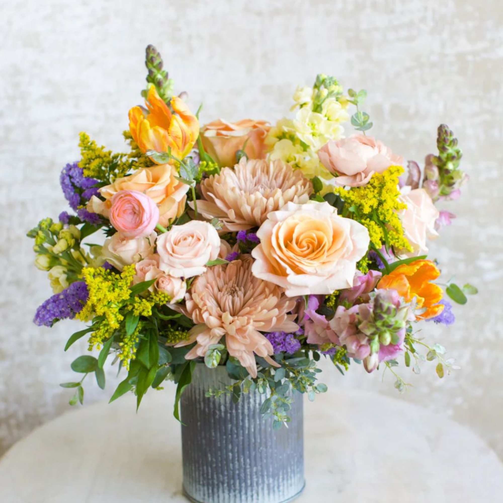 Peach and yellow mixed flower arrangement with roses and mums in a gray metal cylinder vase