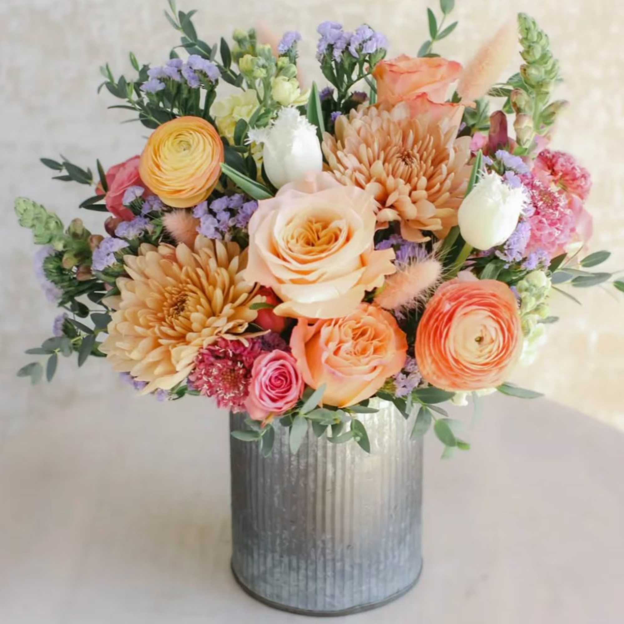 Peach and pink mixed flower arrangement with roses and mums in a ribbed metal vase