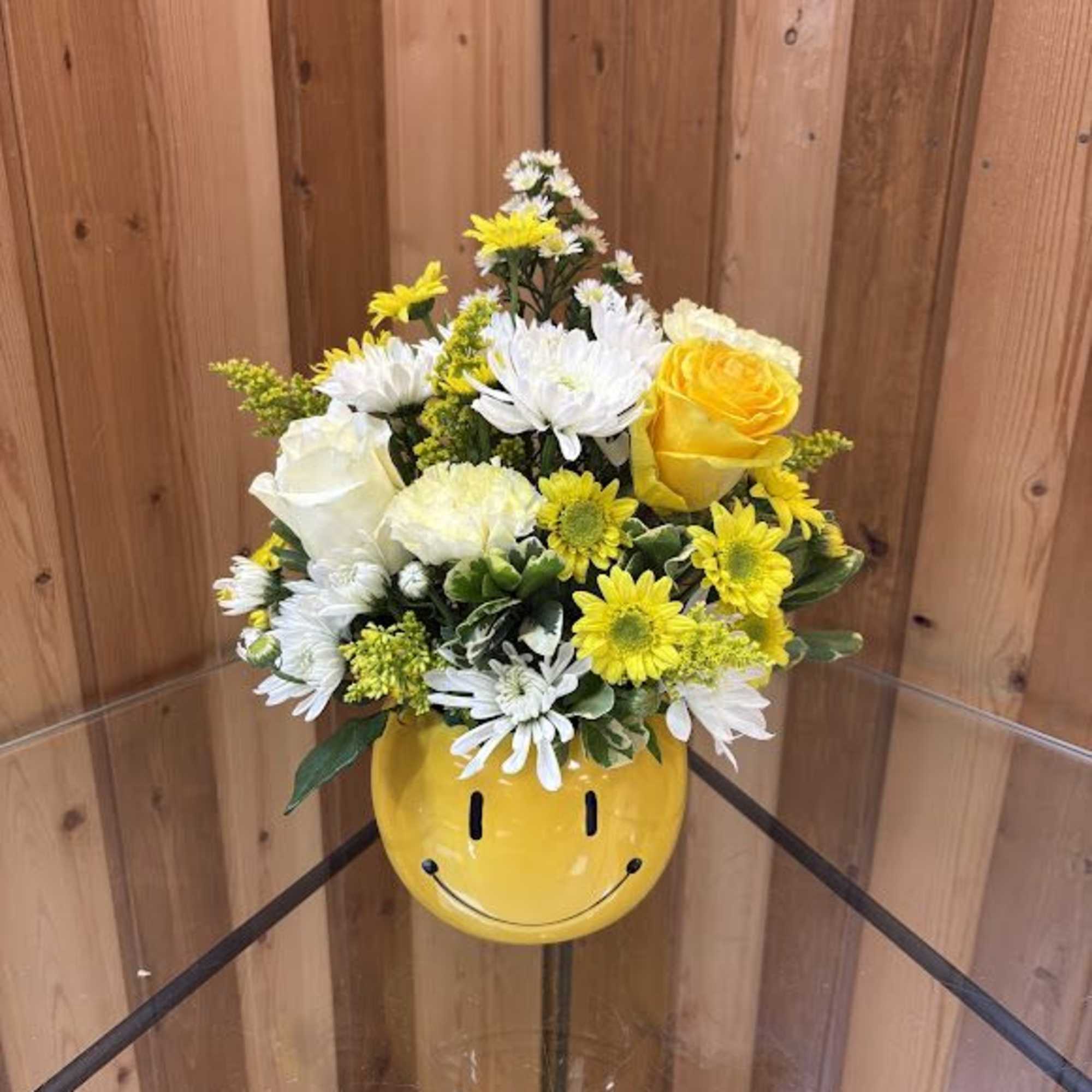Yellow and white mixed flower arrangement in a yellow smiley-face ceramic mug