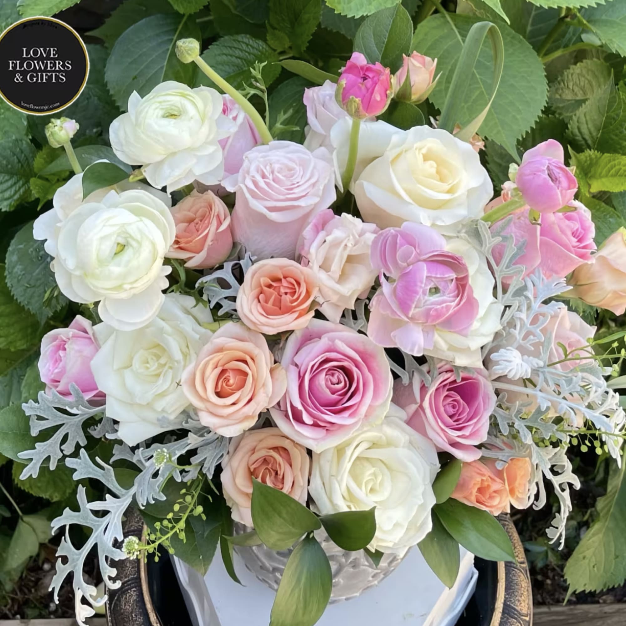 Pastel arrangement of pink, peach, and white roses with ranunculus in a white ceramic vase