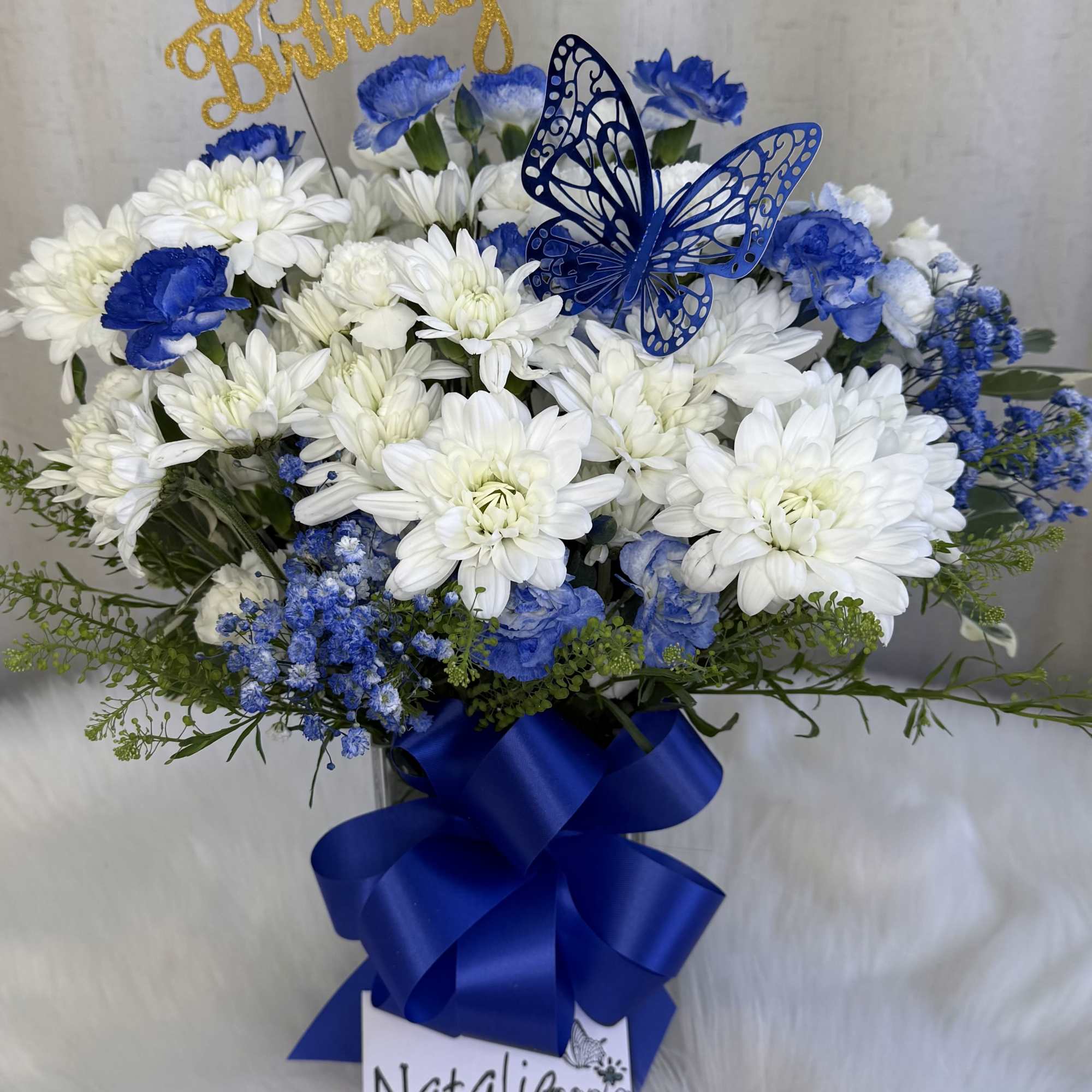Blue and white flower arrangement with a butterfly topper and ribbon