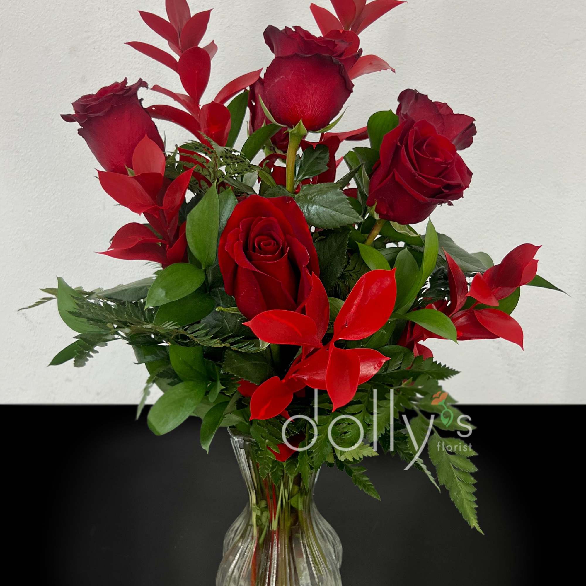 Deep red long-stem roses arranged with glossy red foliage and mixed greenery