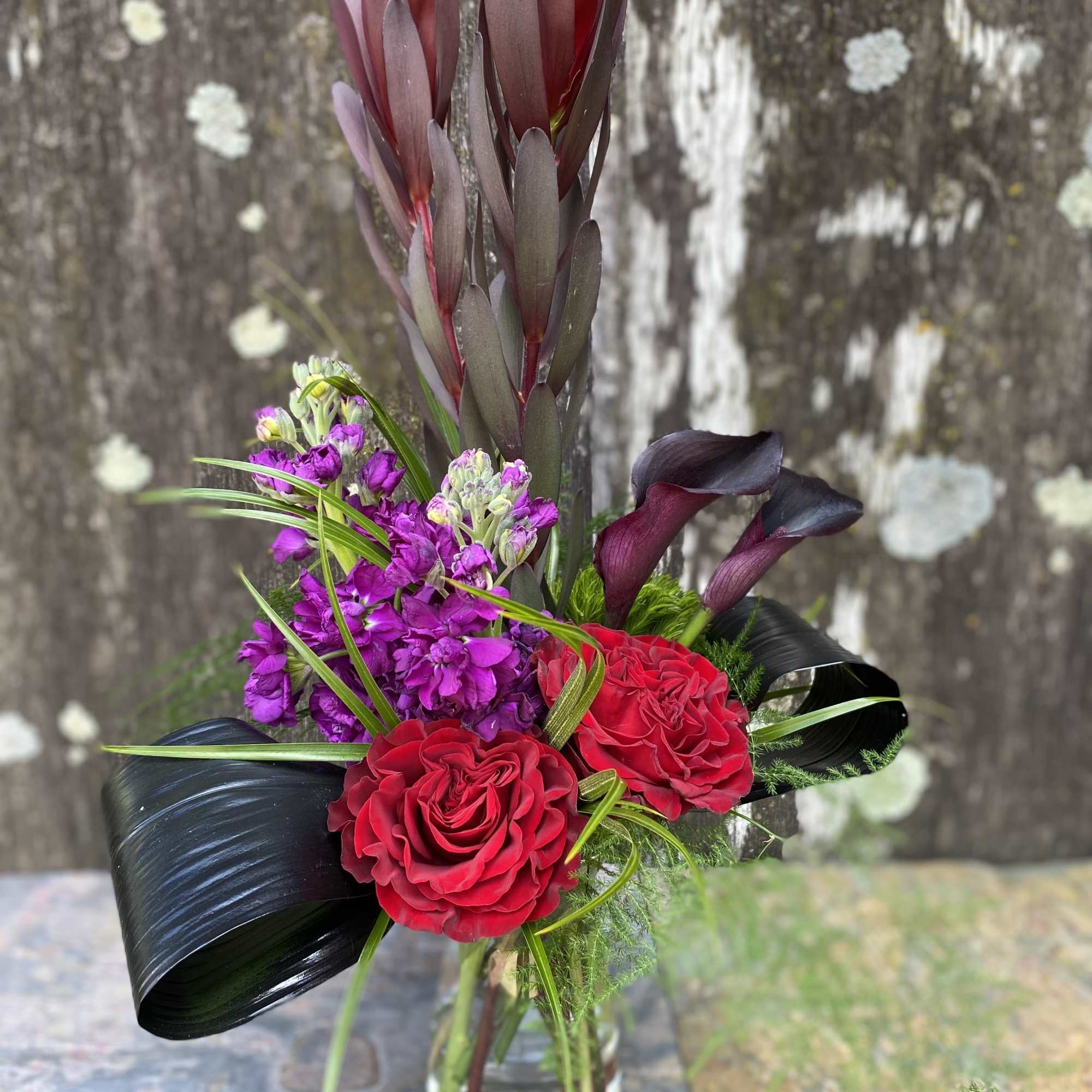 Bouquet of red roses, purple flowers, and dark calla lilies in a glass vase