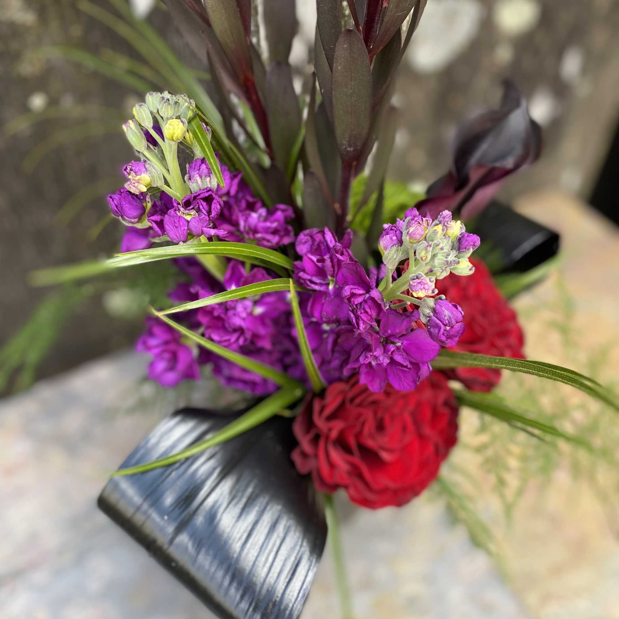 Bouquet of purple and red flowers with dark foliage and black wrap