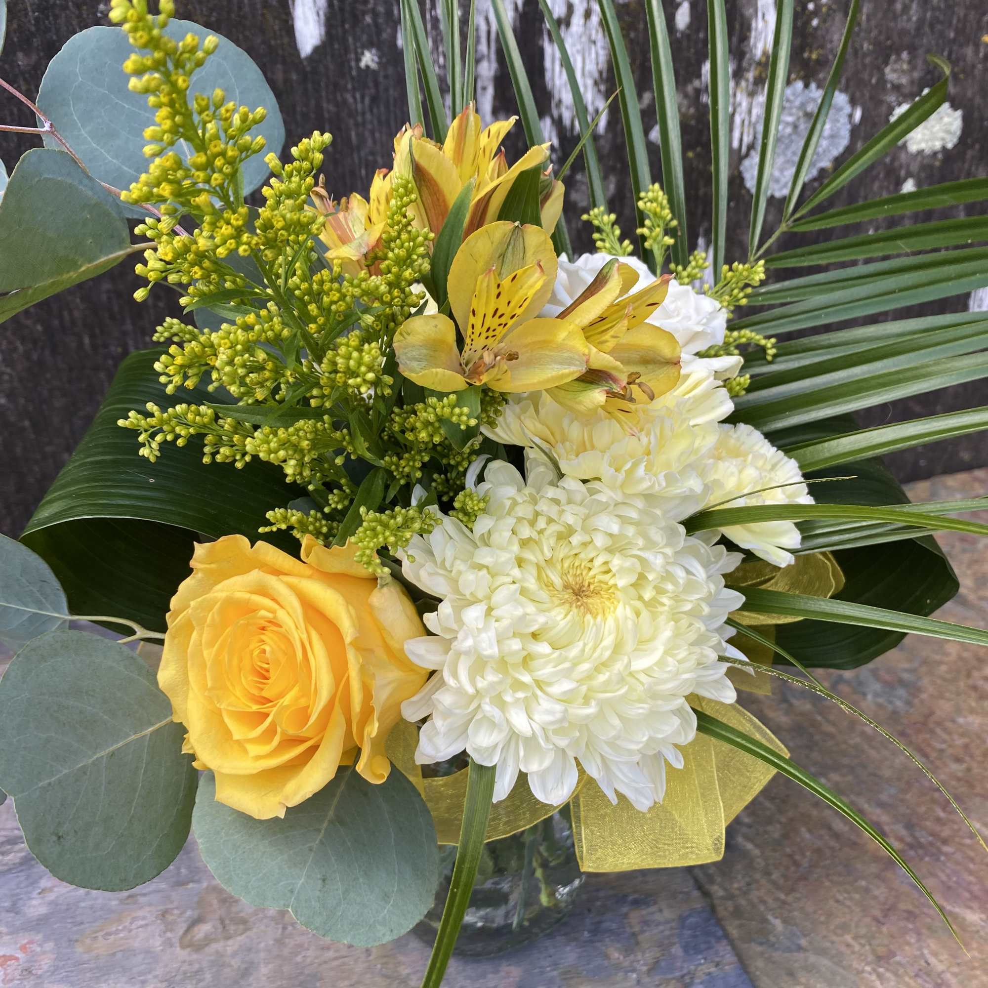 Yellow roses and white chrysanthemums with tropical foliage in a glass vase