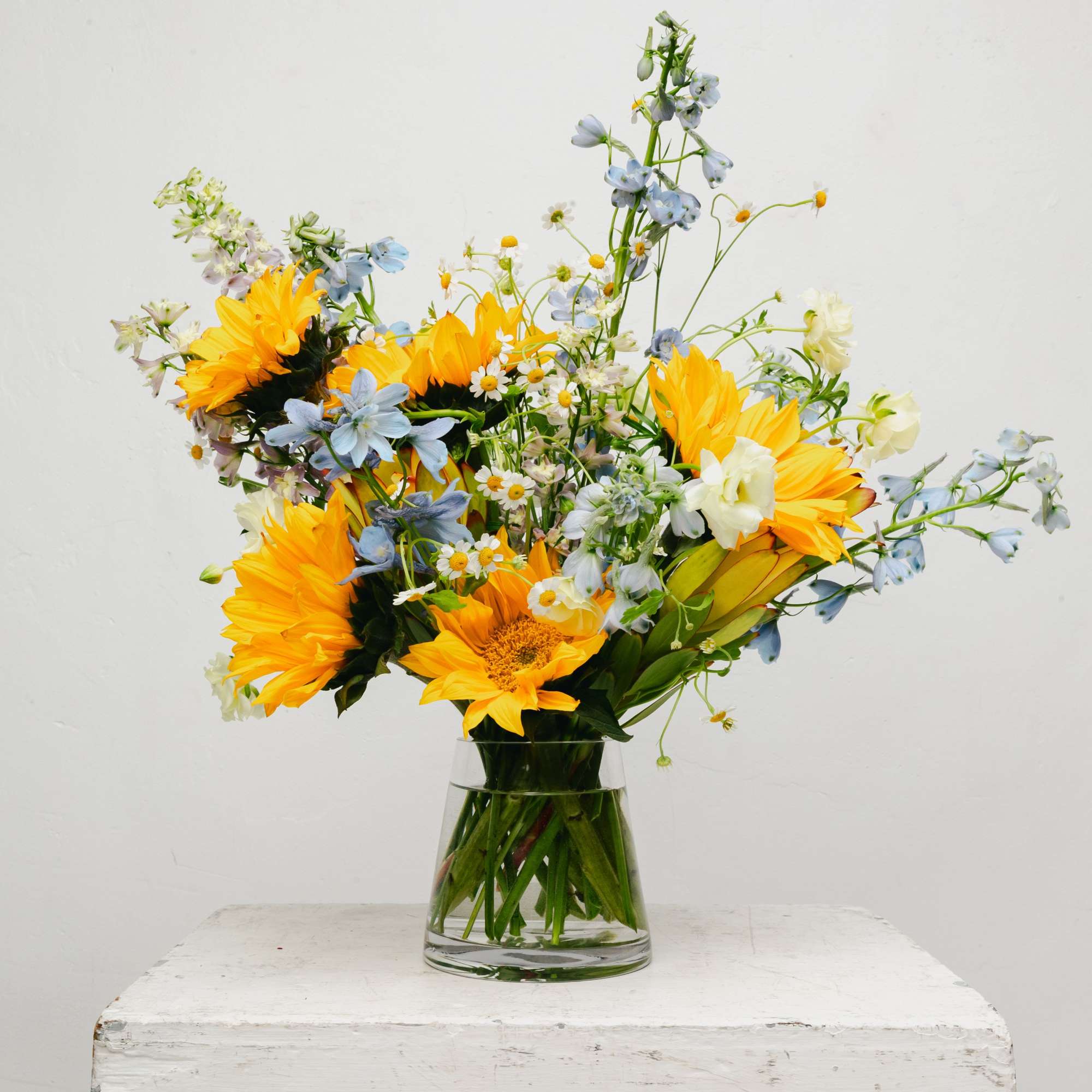 Brighten your space with our enchanting Sunflower and Blue Delphinium flower arrangement