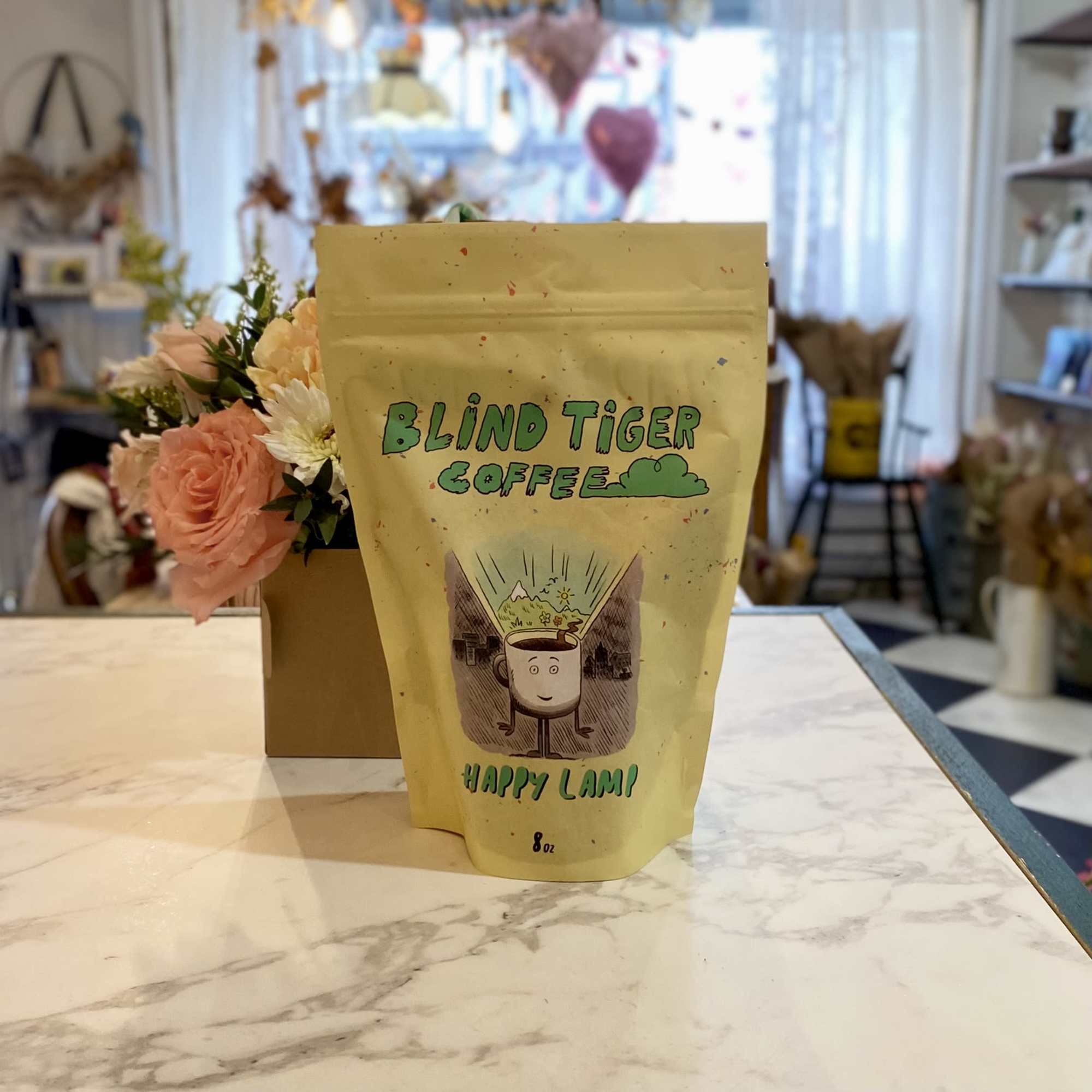 Coffee bag with a small peach flower arrangement behind it