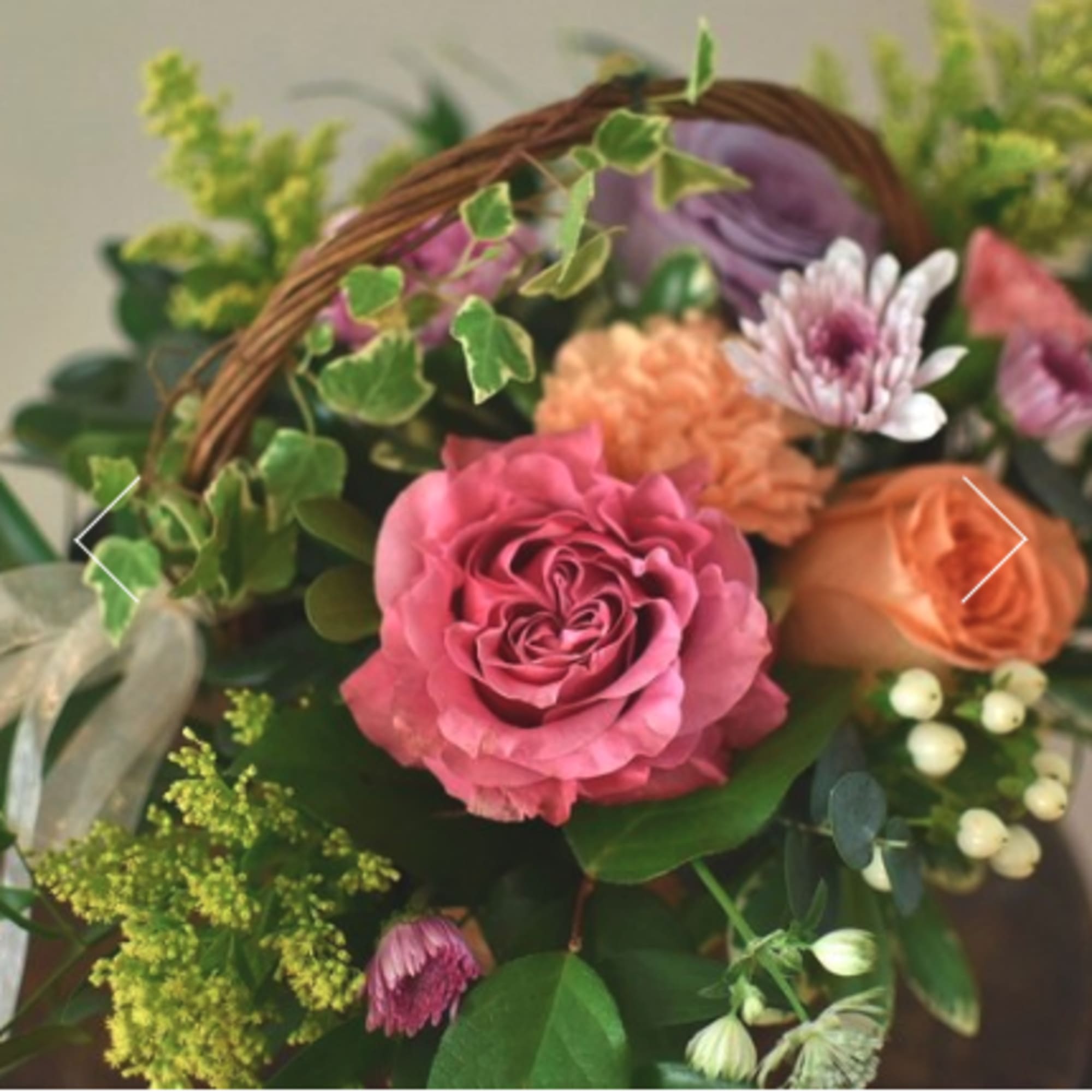 Basket arrangement with pink and peach roses and purple blooms