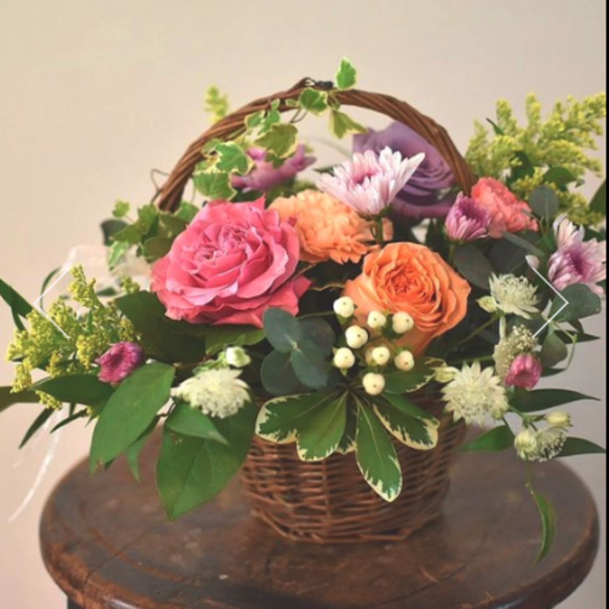 Basket arrangement of pink and orange roses with purple blooms