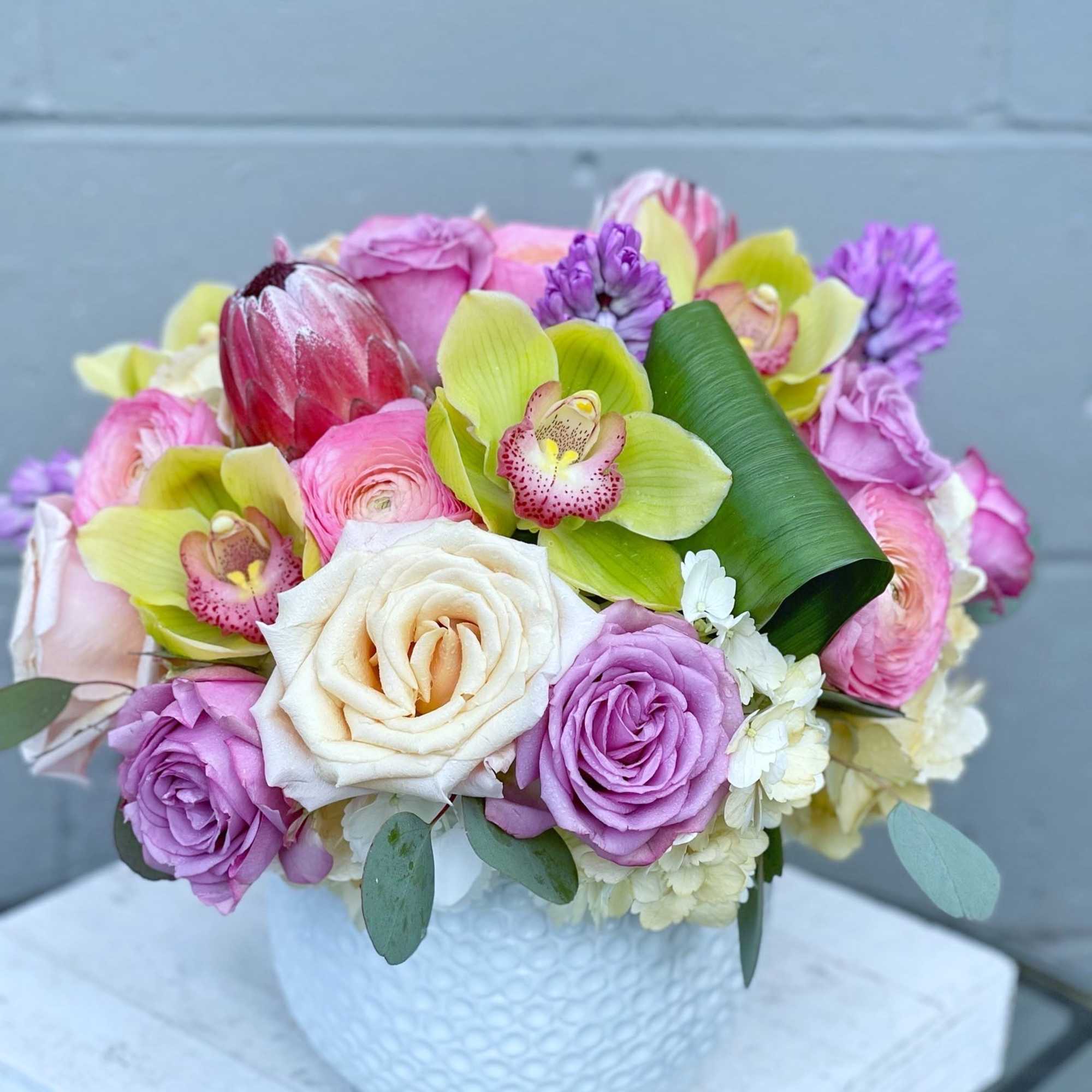 Bouquet of pink and lavender roses with orchids in a white vase