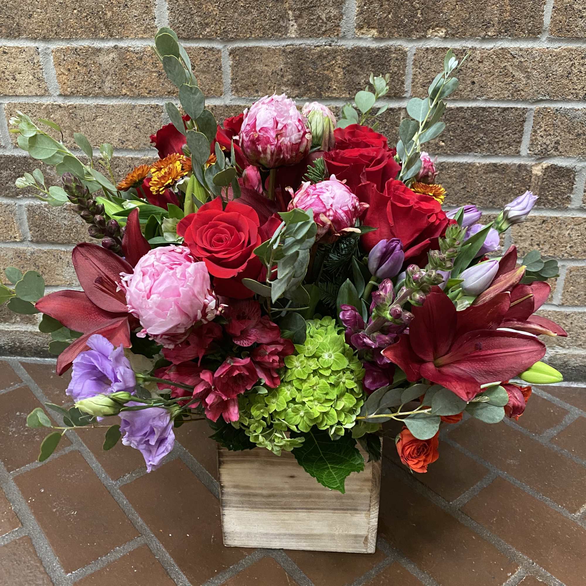 Mixed bouquet of red roses, pink blooms, and purple flowers in a wooden box