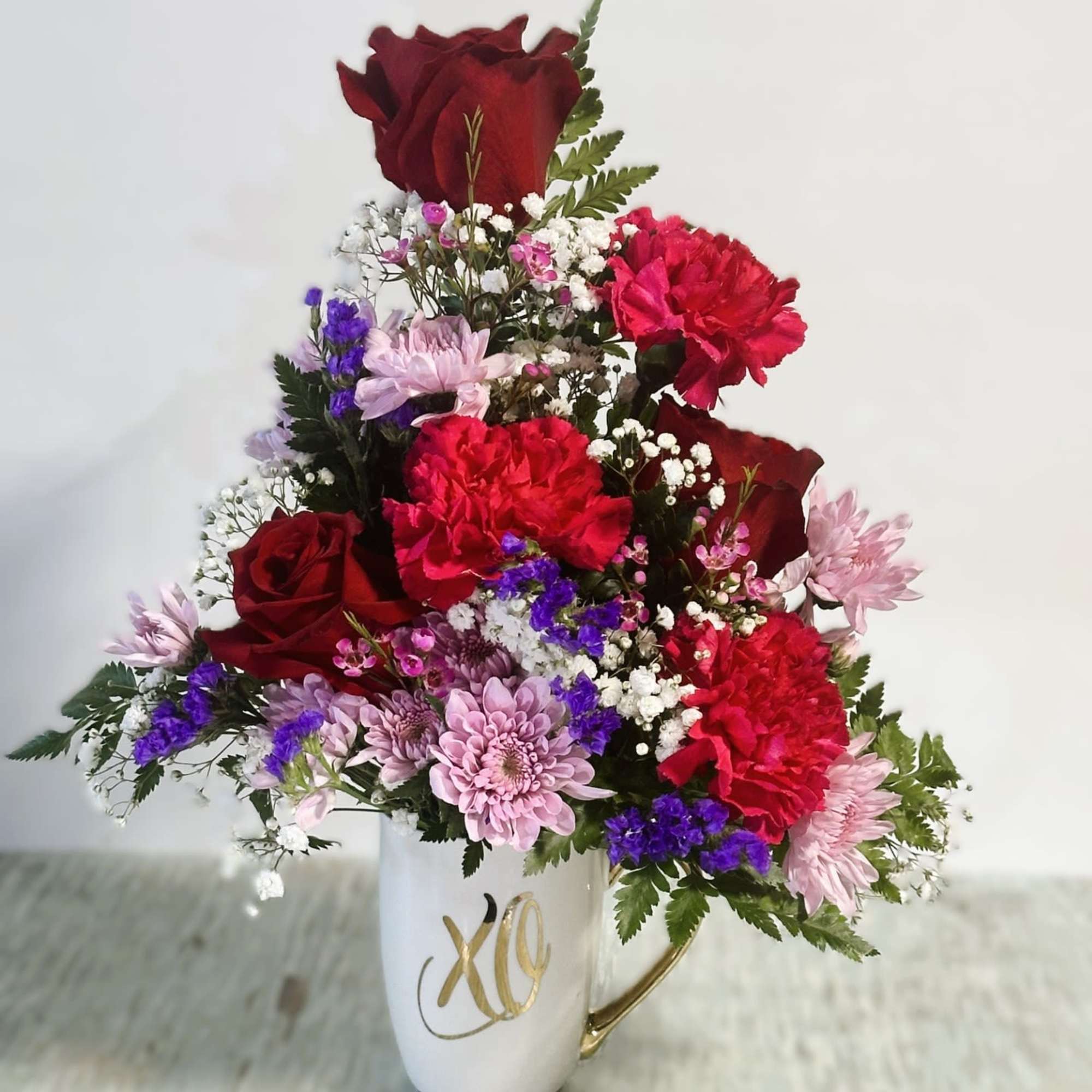 Mixed red, pink, and purple flowers arranged in a white mug vase