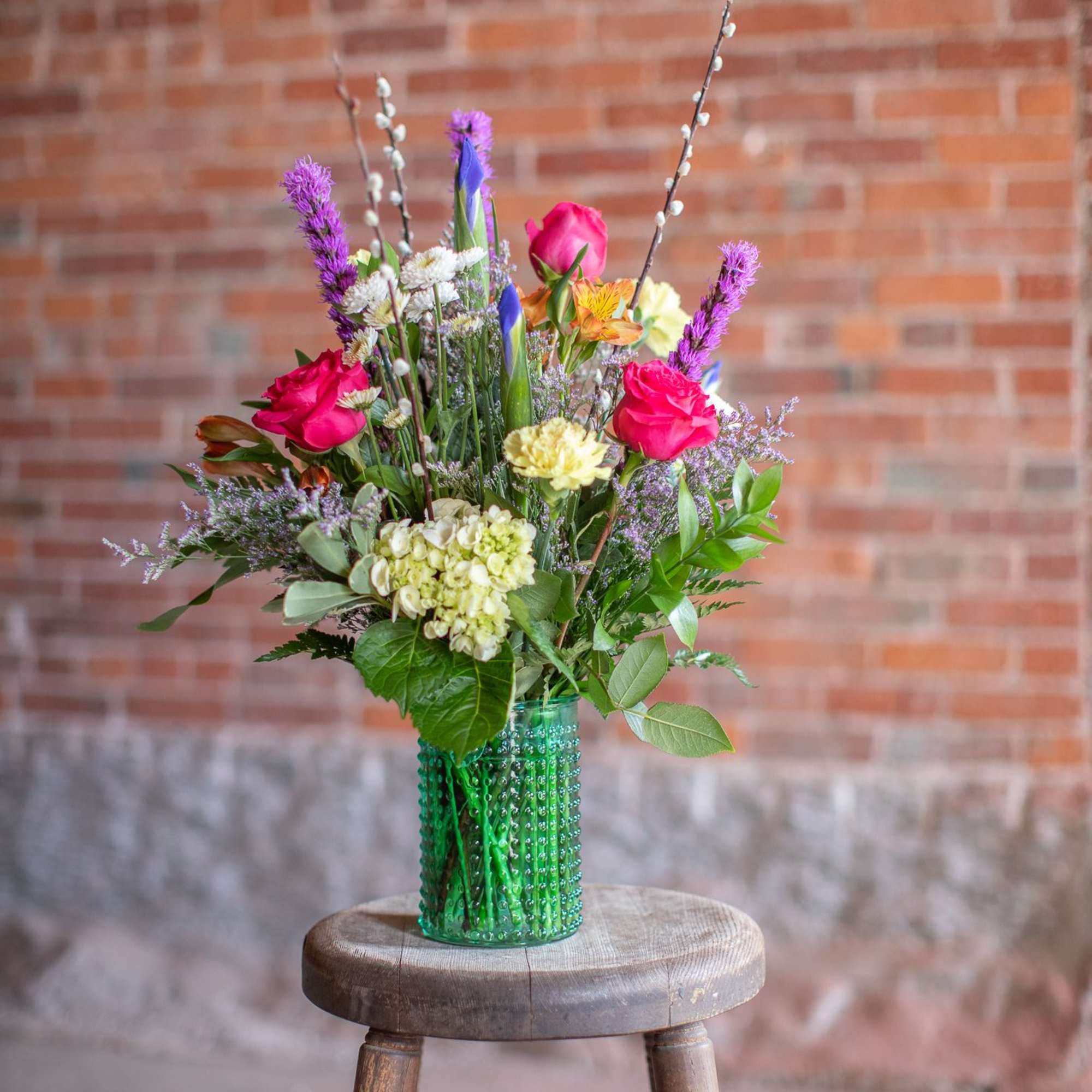 Mixed bouquet of pink roses and purple flowers in a green glass vase