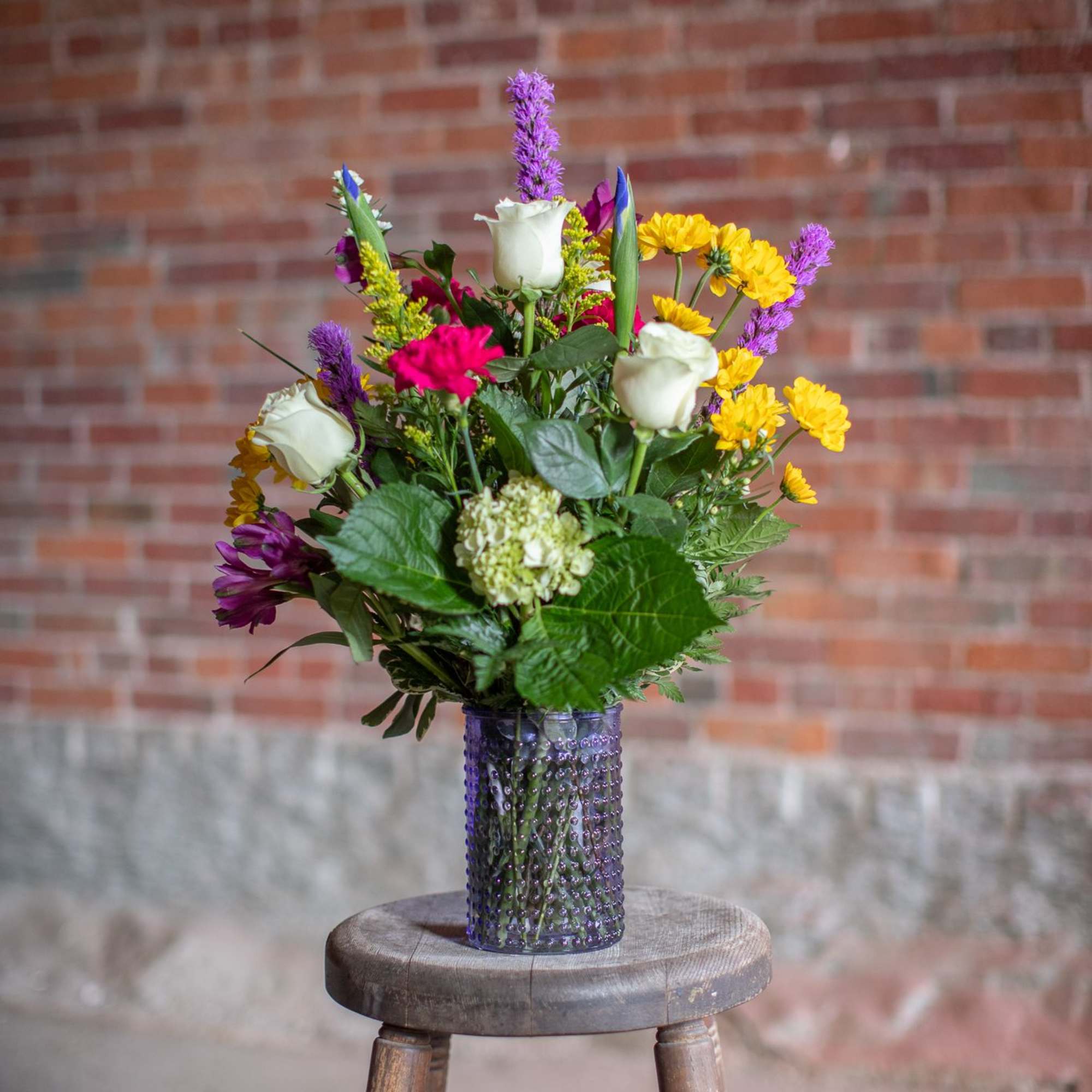 Mixed bouquet of white roses, yellow daisies, and purple flowers in a glass vase